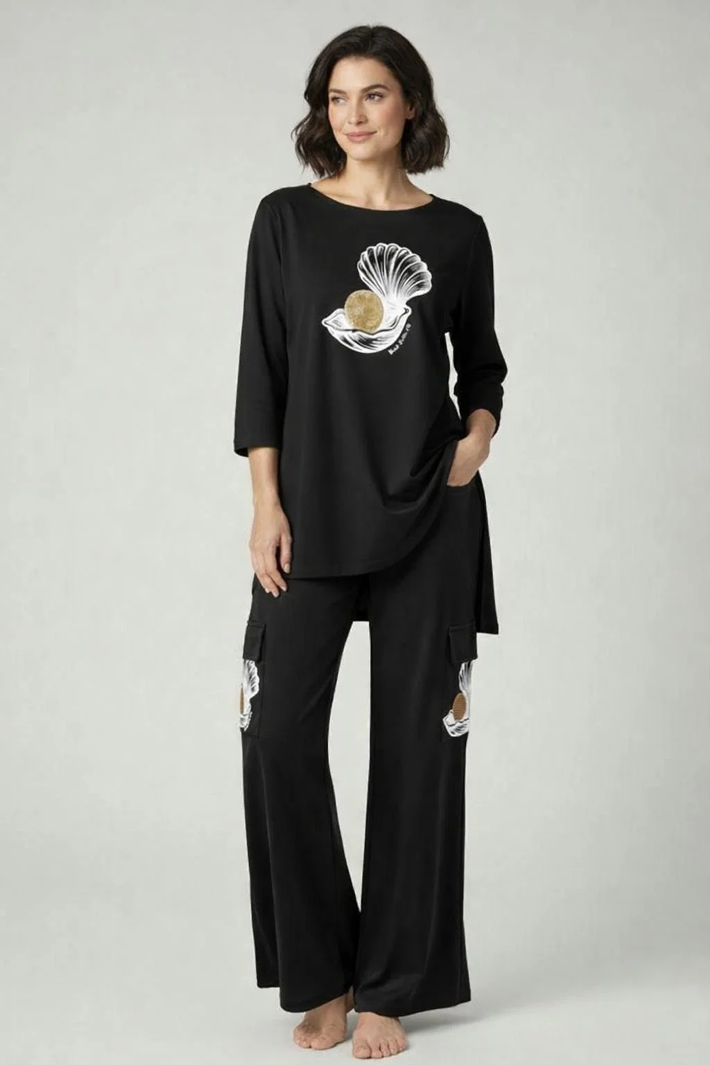 A woman in black loungewear with a shell and ball graphic on the top and ripped details on the pants, standing against a plain background.