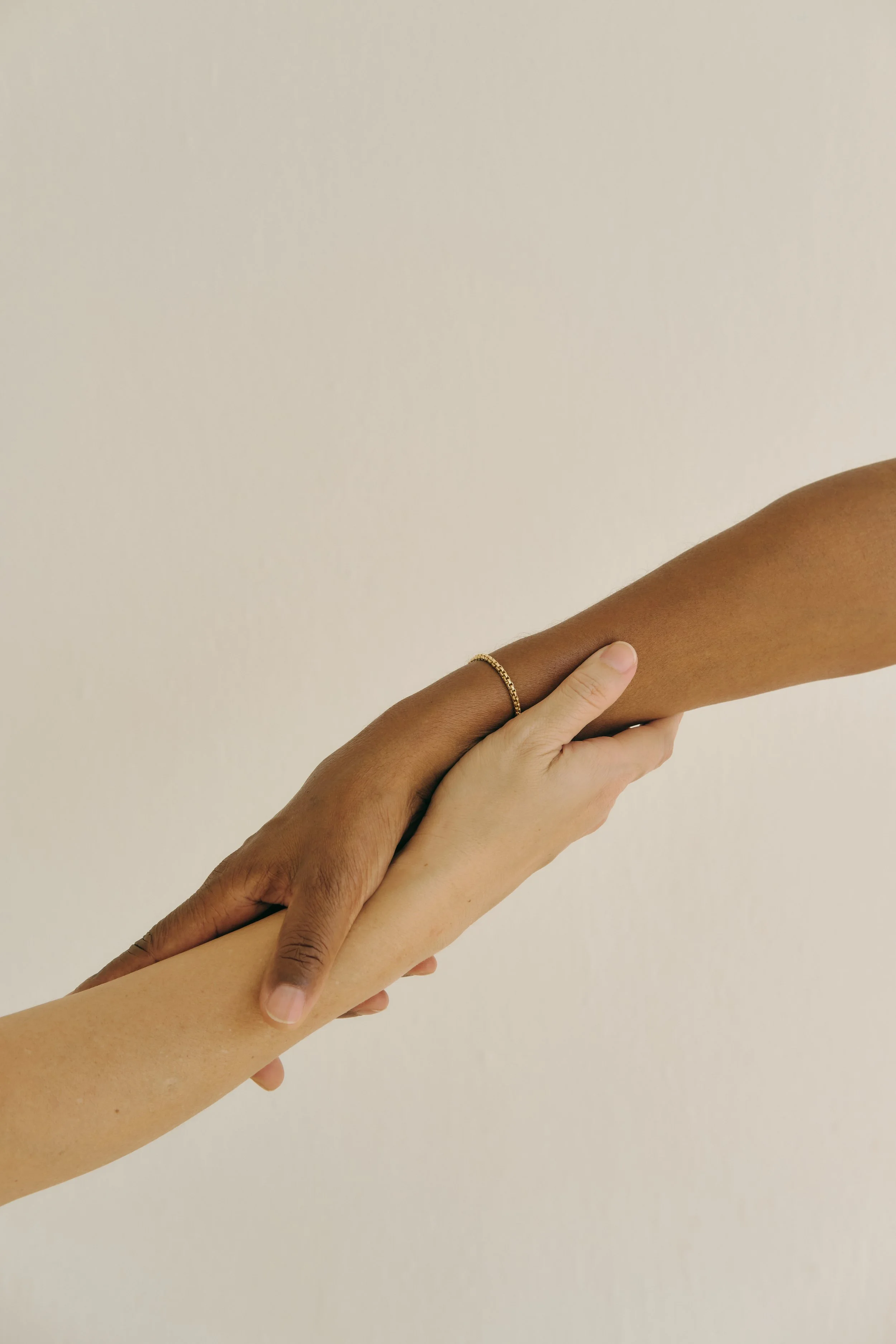Two hands, one light-skinned and one dark-skinned, gently holding each other's arms against a plain background.