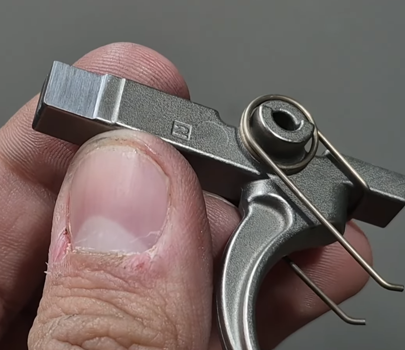 Close-up of a person's hand holding a properly cut milspec trigger for a super selector to function properly. Material is removed to allow clearance and perfect function in forced reset mode.