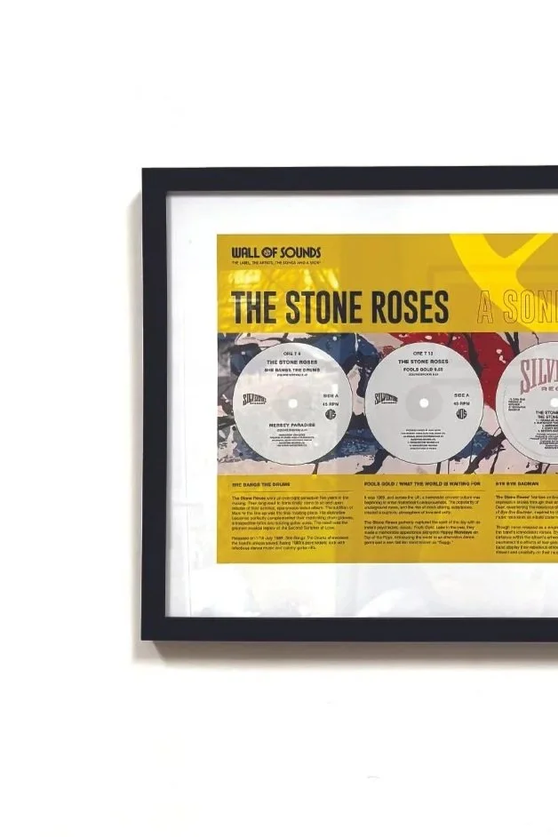 Framed display of vinyl record album cover and information about The Stone Roses band and their album 'The Stone Roses' on a white wall.