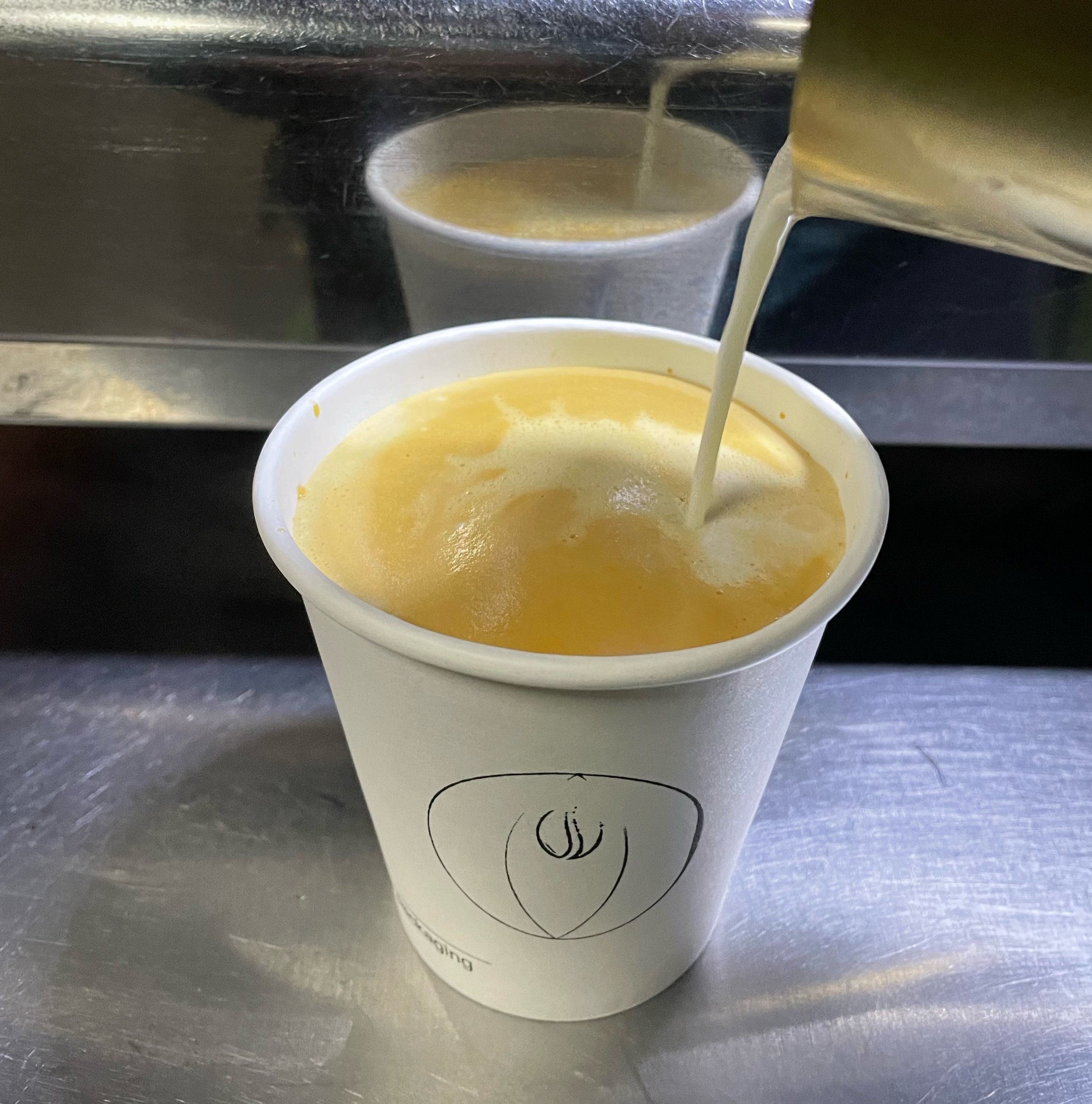 A white compostable paper cup with the Lesbean & Co logo is being filled with a coffee.