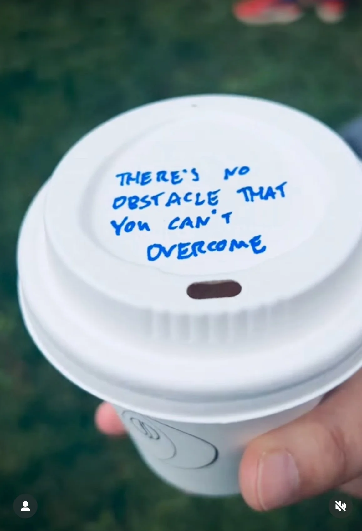 A white disposable coffee cup with a handwritten message on the lid in blue ink that says, 'There's no obstacle that you can't overcome.'
