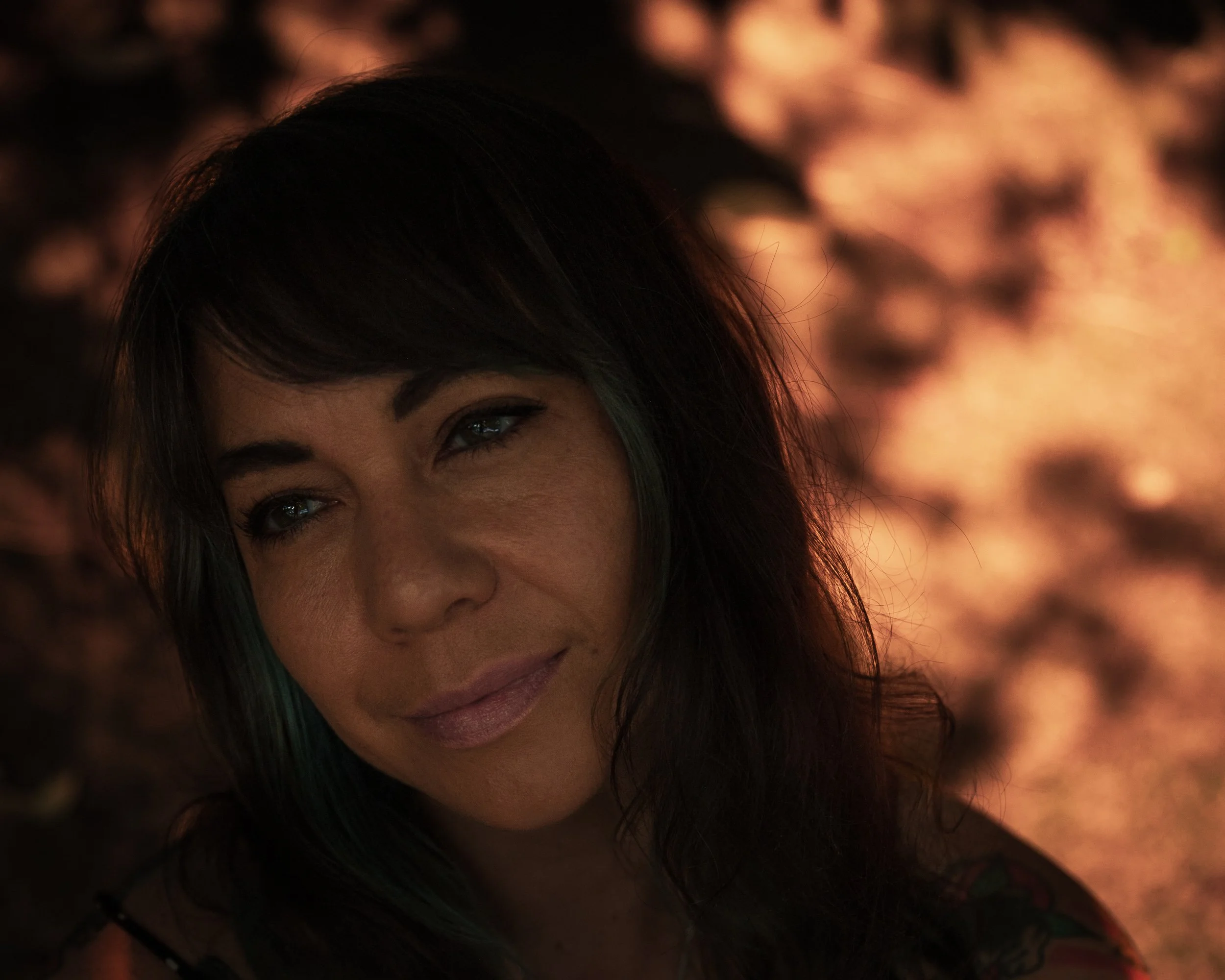 Close-up of a woman's face, half-visible, with dark hair and a subtle smile, against a warm, bokeh background.