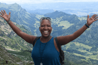 Smiling woman with arms outstretched in front of a mountainous landscape during daytime