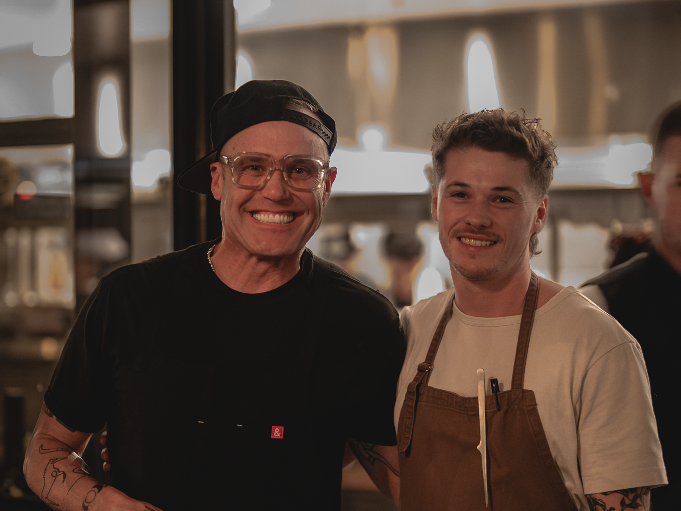 Chef Aidan Owens smiling with Brian Malarkey in front of the kitchen