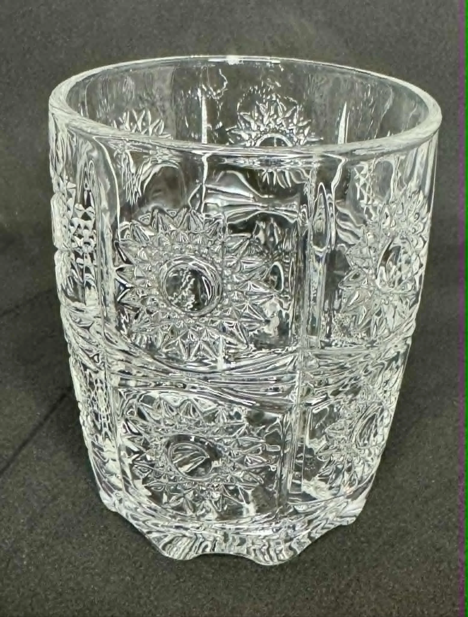 A clear, decorated glass with intricate patterns and designs, sitting on a dark surface.
