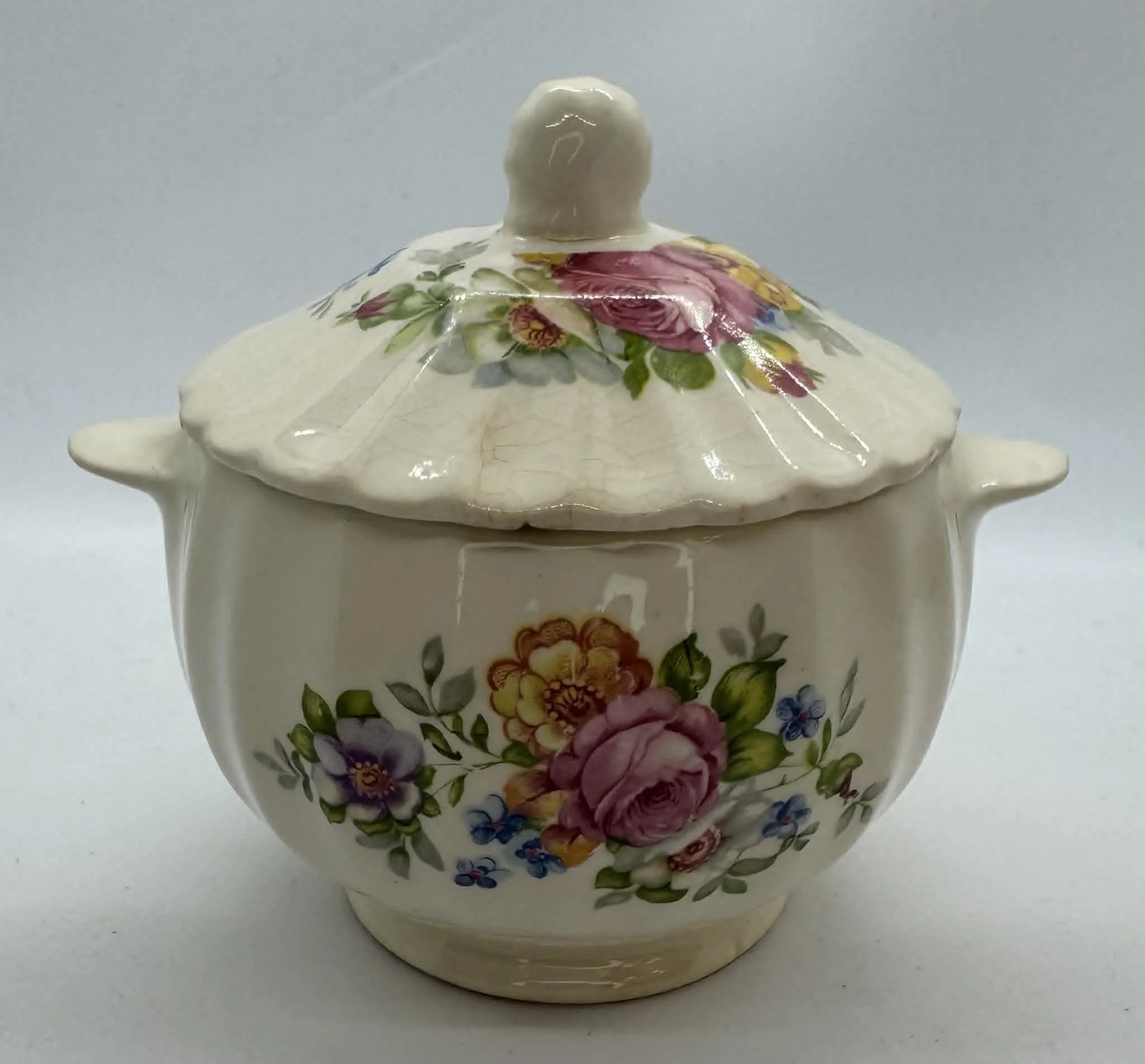 A ceramic sugar bowl with a floral pattern and a lid, placed on a white surface.