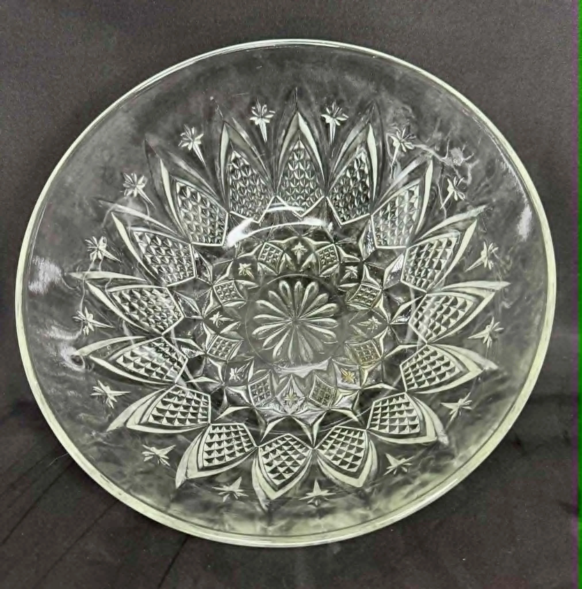 A clear cut glass bowl with intricate floral and geometric patterns etched on its surface, placed on a dark wooden surface.