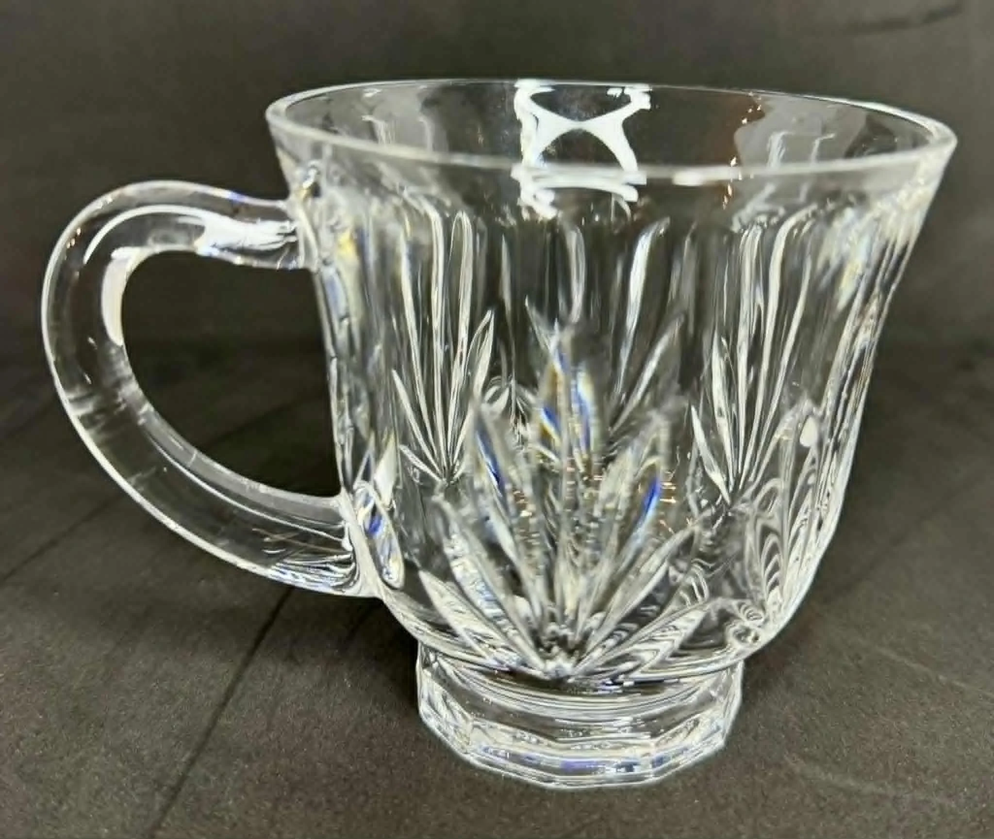 A clear glass teacup with a decorative pattern on a dark surface.