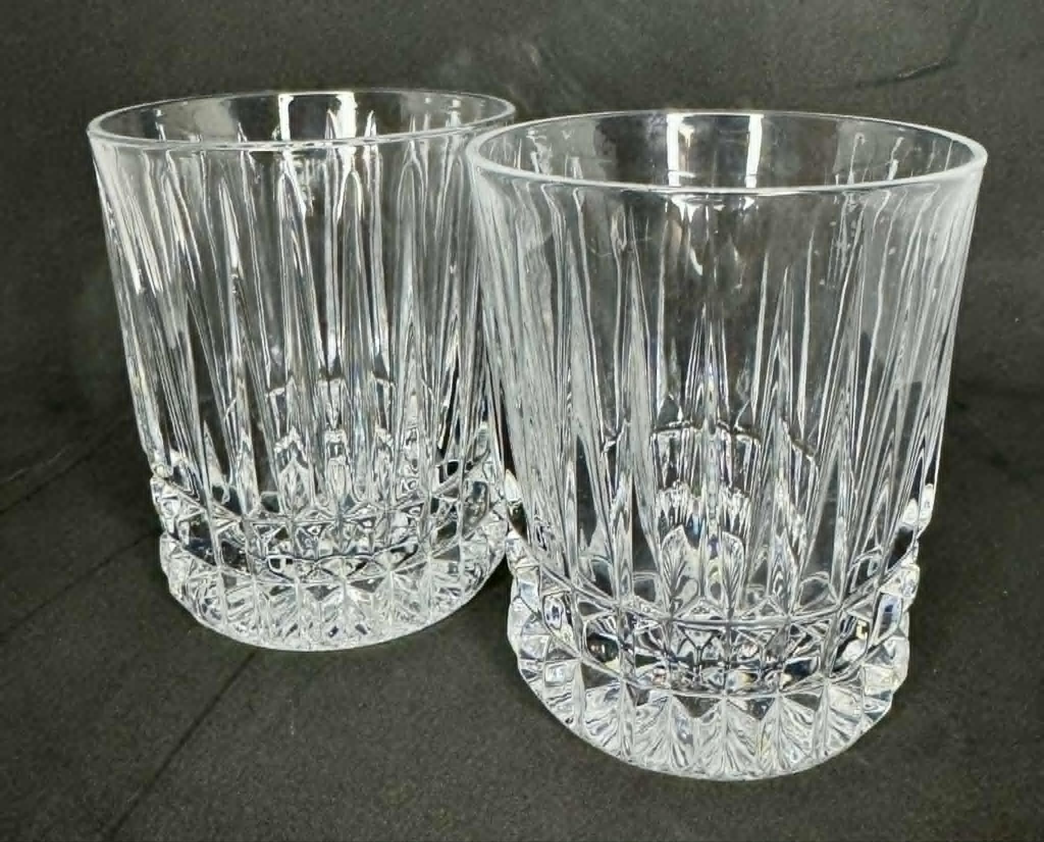 Two empty, clear crystal glasses with intricate geometric patterns on the surface, set against a dark background.