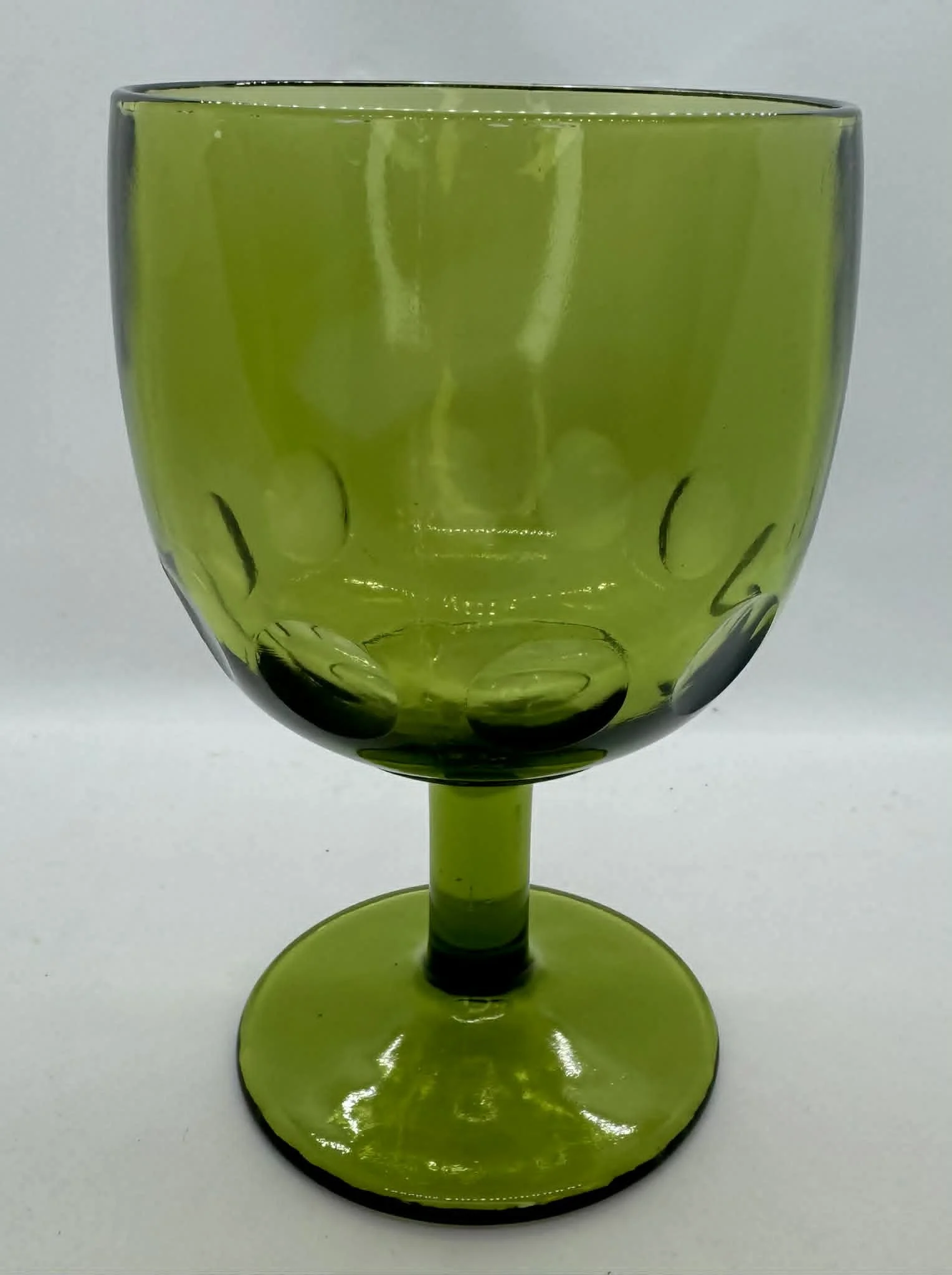 A green glass goblet with a decorative pattern of black dots and crescent shapes, set against a plain white background.