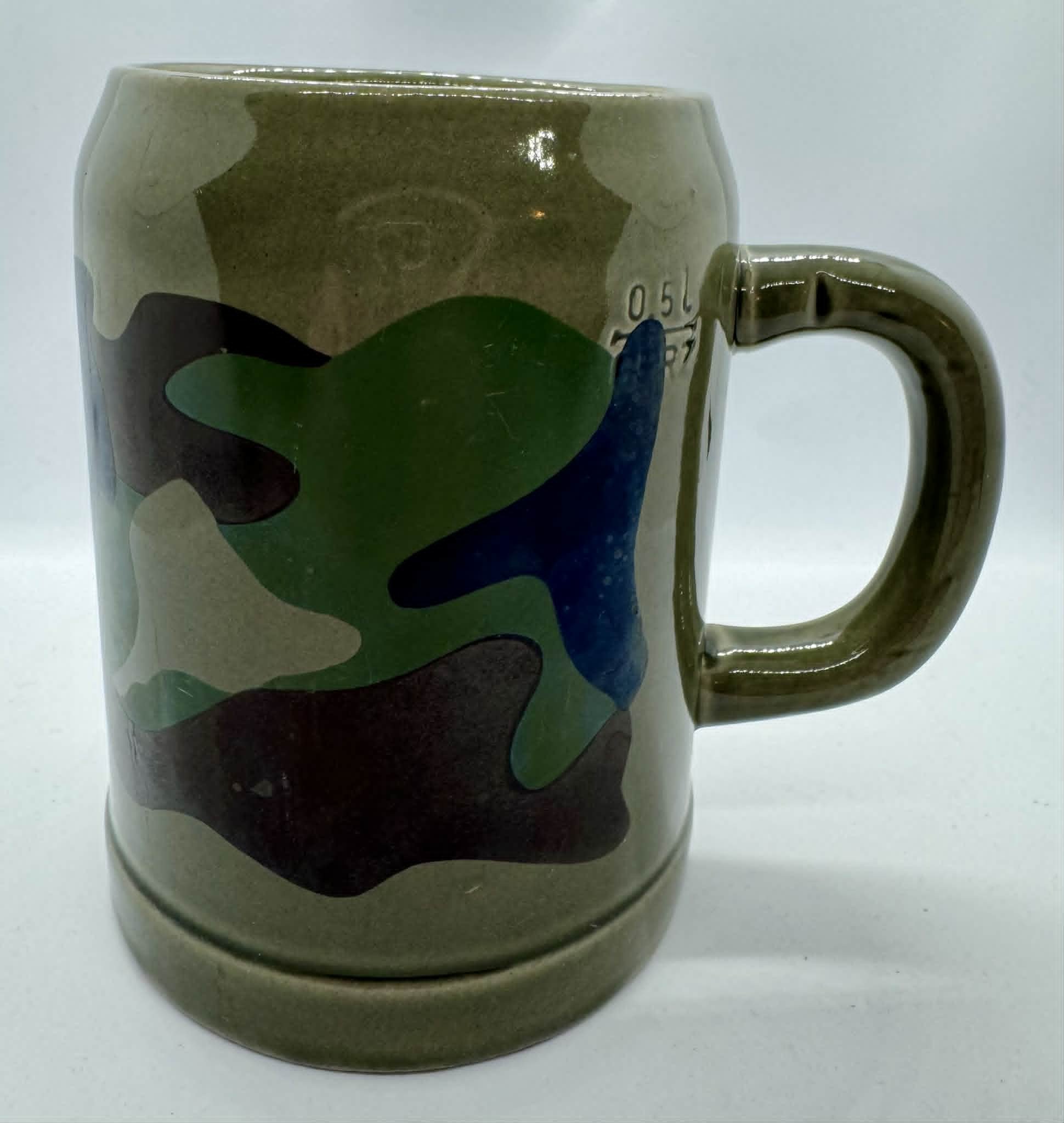 A ceramic mug with a colorful abstract design featuring shades of green, blue, brown, and black on a white background.