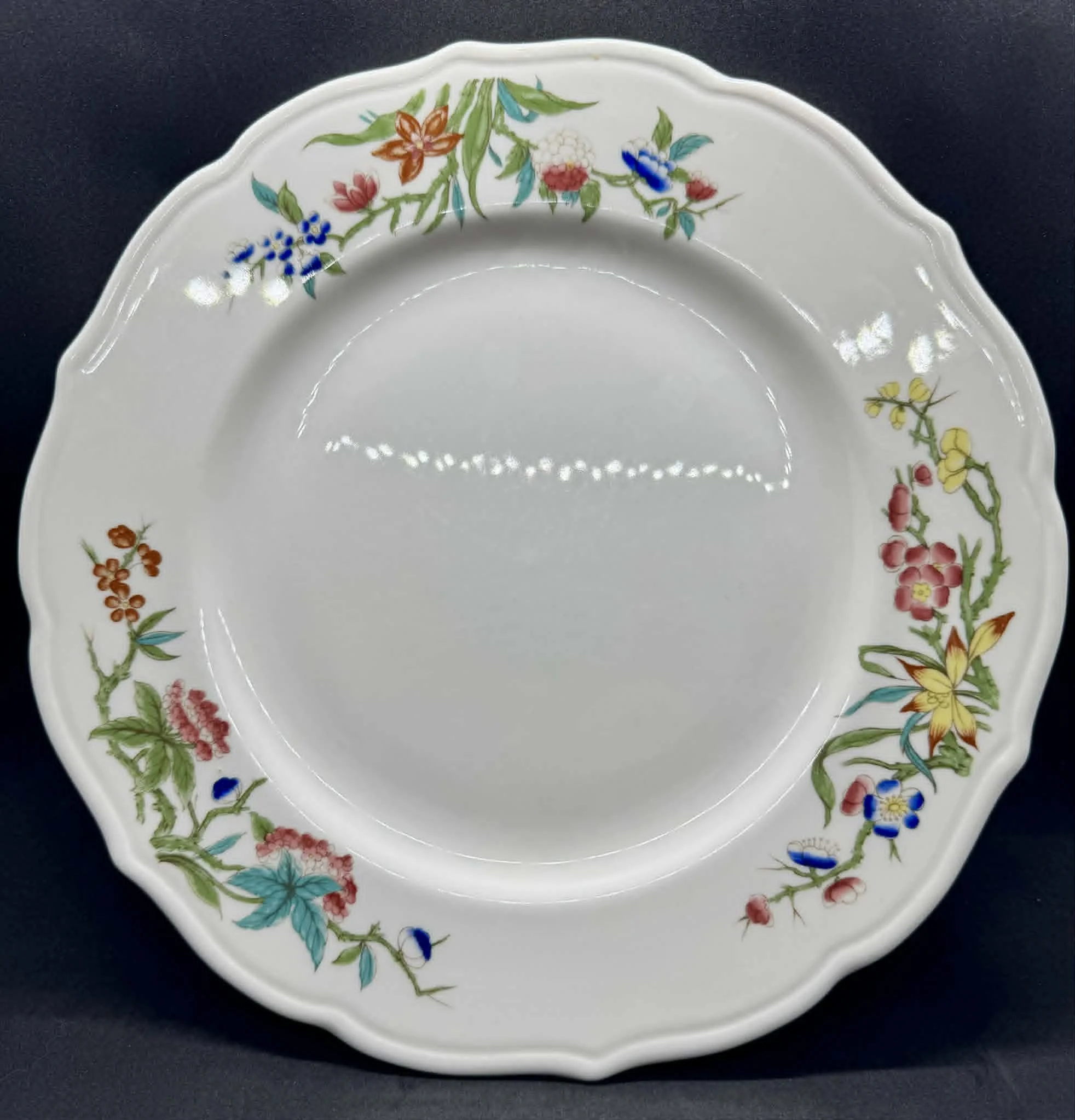 Decorative porcelain plate with floral pattern, featuring colorful flowers and green leaves, on a black background.