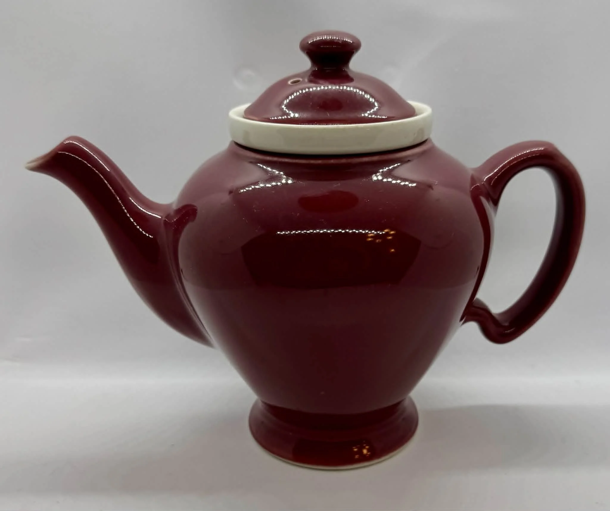 Red teapot with white lid, captured against a plain gray background.