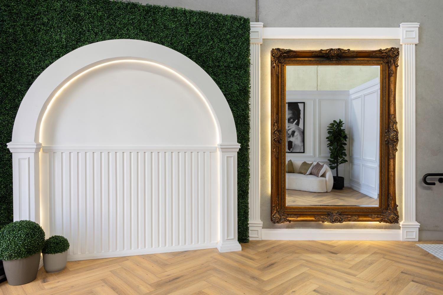 Interior with large ornate mirror, decorative arch with LED lighting, artificial greenery, and herringbone wood floor..jpg