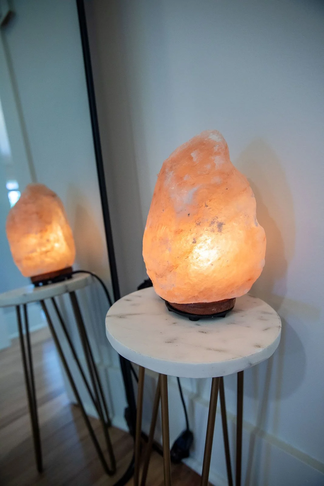 Himalayan salt lamps on small round tables in a room with hardwood floors.