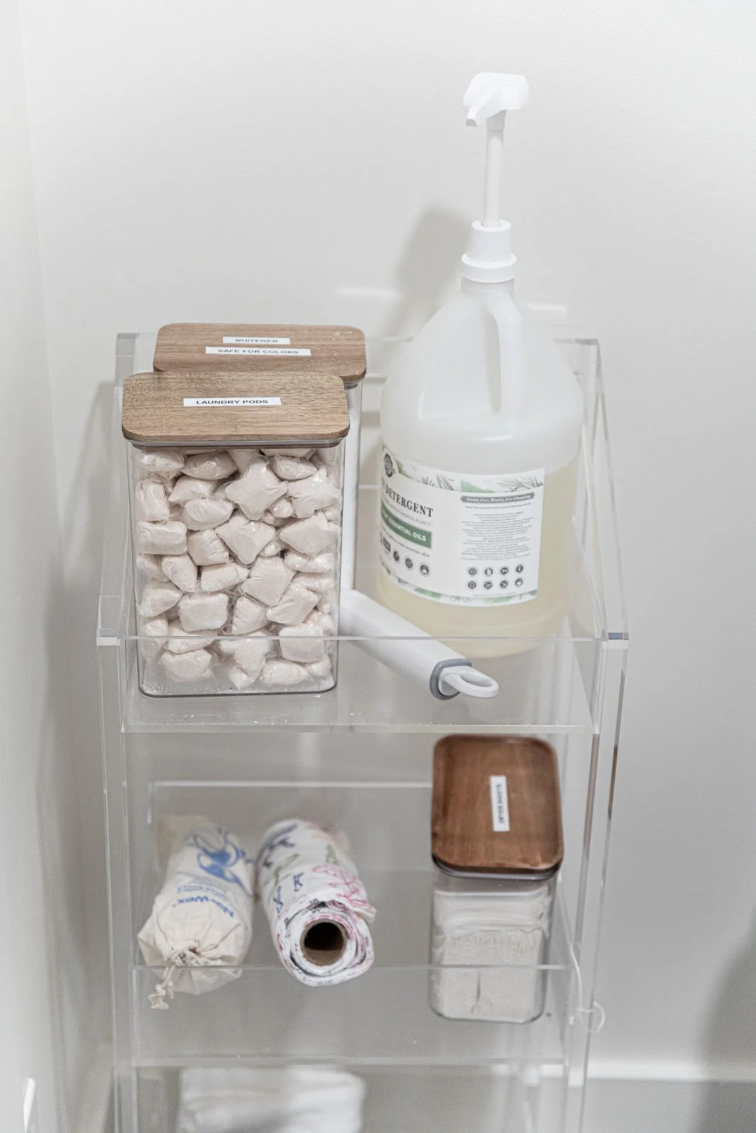 A clear plastic organizer with labels, containing laundry supplies such as detergent, laundry pods, soap, and fabric softener bottles.