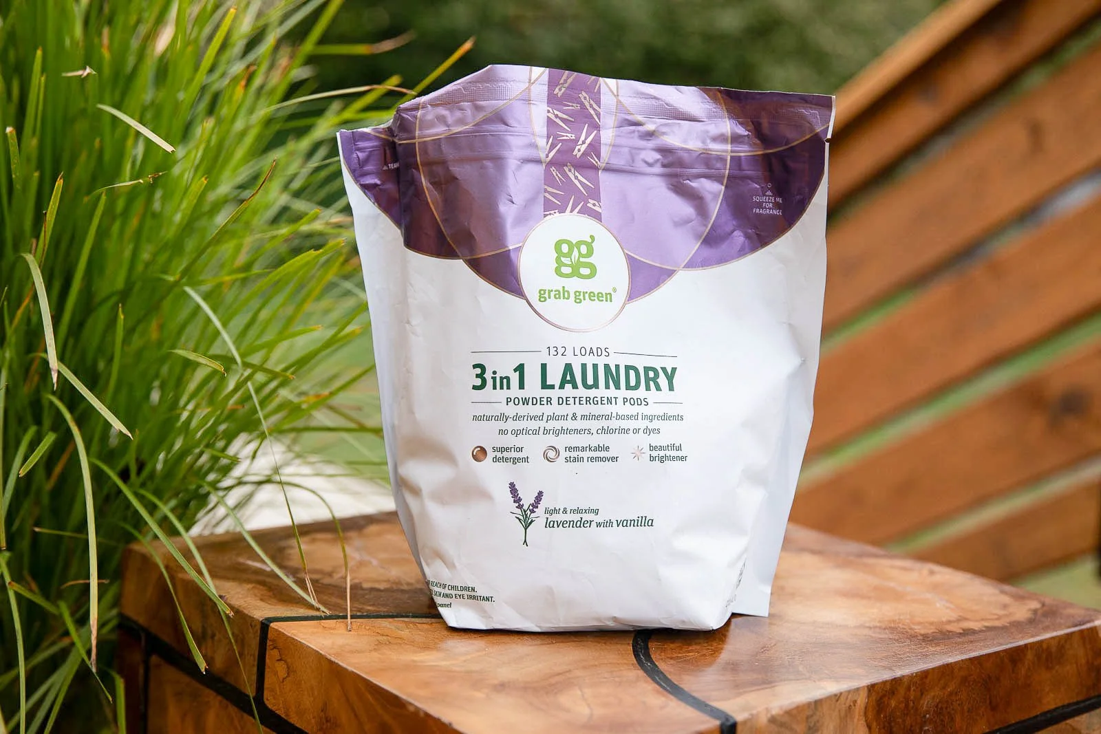 Bag of Grab Green 3-in-1 laundry powder detergent pods with lavender and vanilla scent, placed on a wooden surface outdoors.