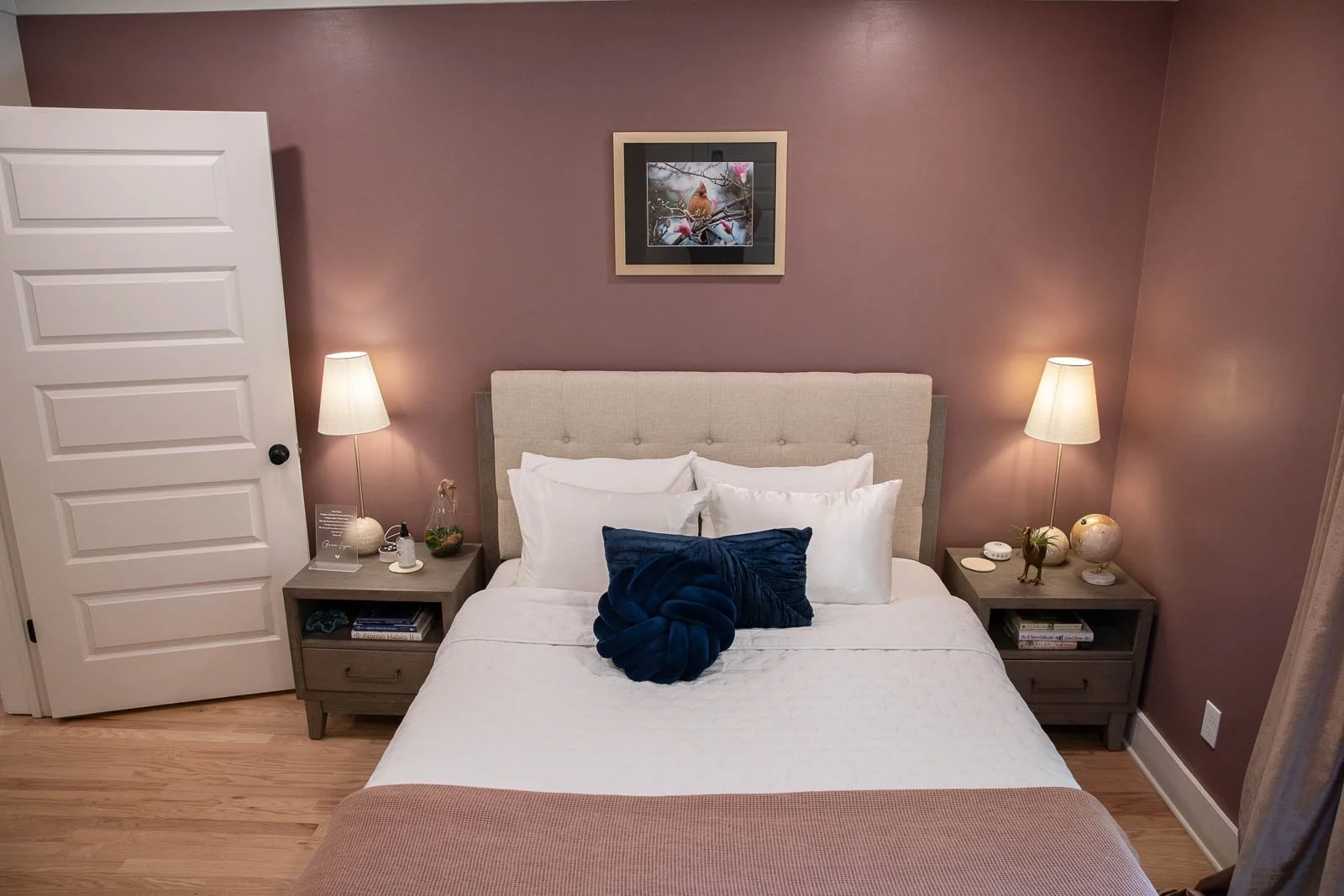 A bedroom with a bed, two nightstands with lamps, and artwork of a bird on the wall.