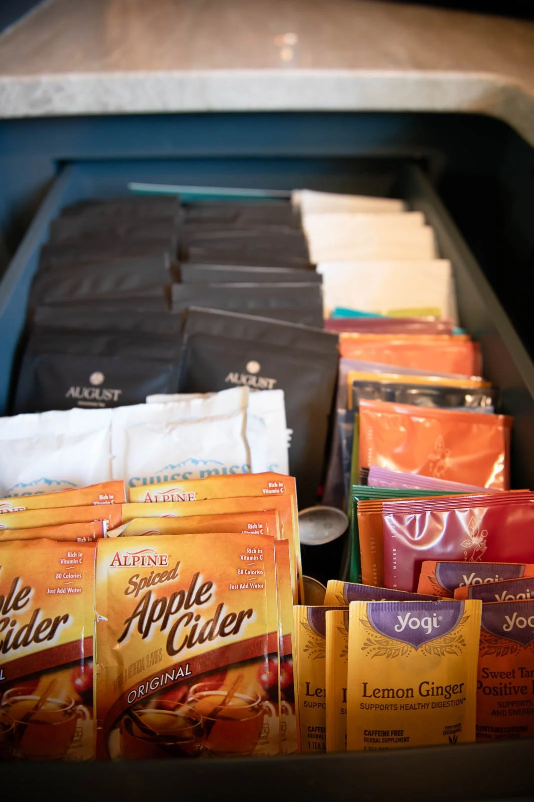 A drawer filled with packets of tea, including Alpine spiced apple cider, Yogi lemon ginger, and other assorted tea brands.