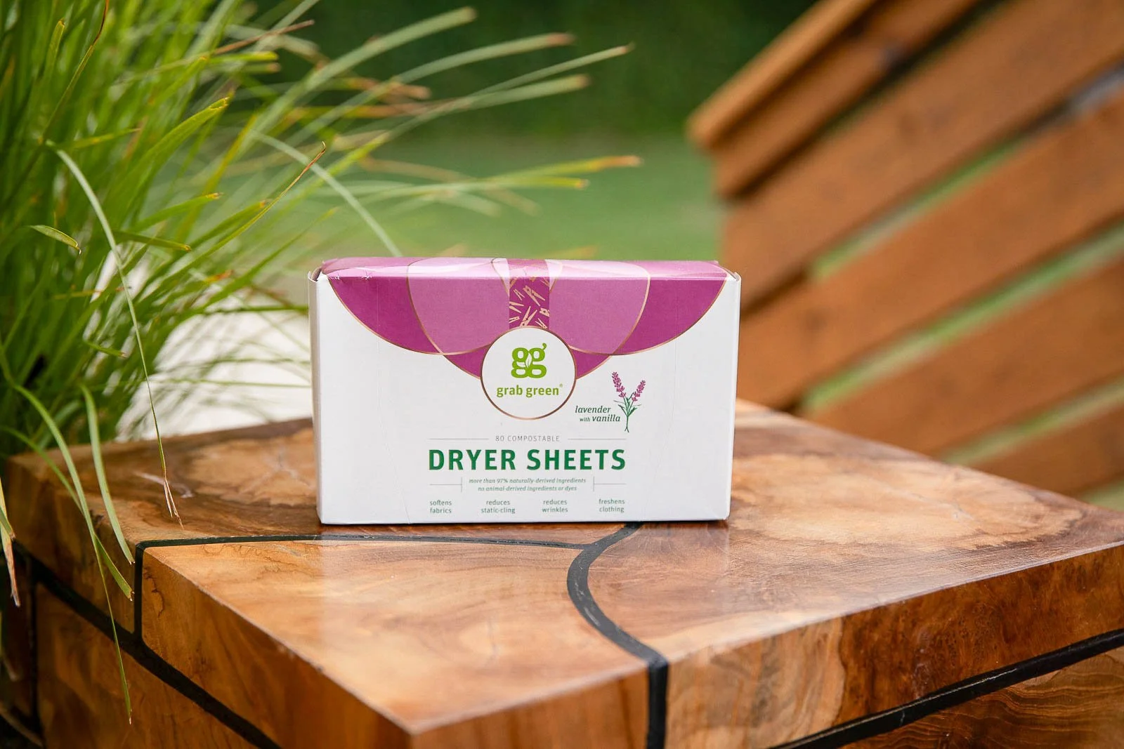 A box of Grab Green lavender and vanilla dryer sheets on a wooden surface outdoors, with green plants in the background.