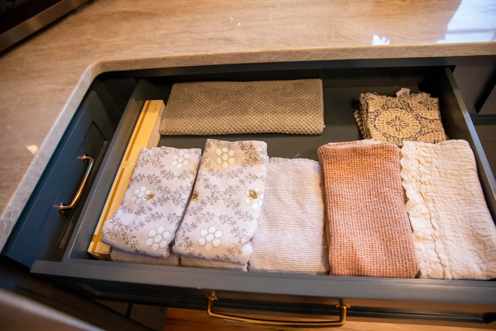Open drawer containing neatly folded towels of various patterns and colors, with a ruler and a textured mat inside.