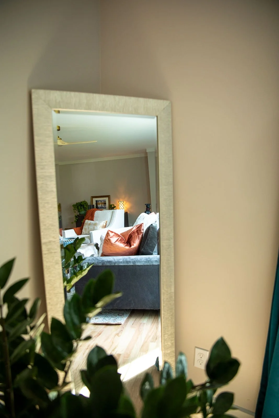Living room reflecting in a wall mirror, with couches, pillows, a small table, and a lamp in the background.