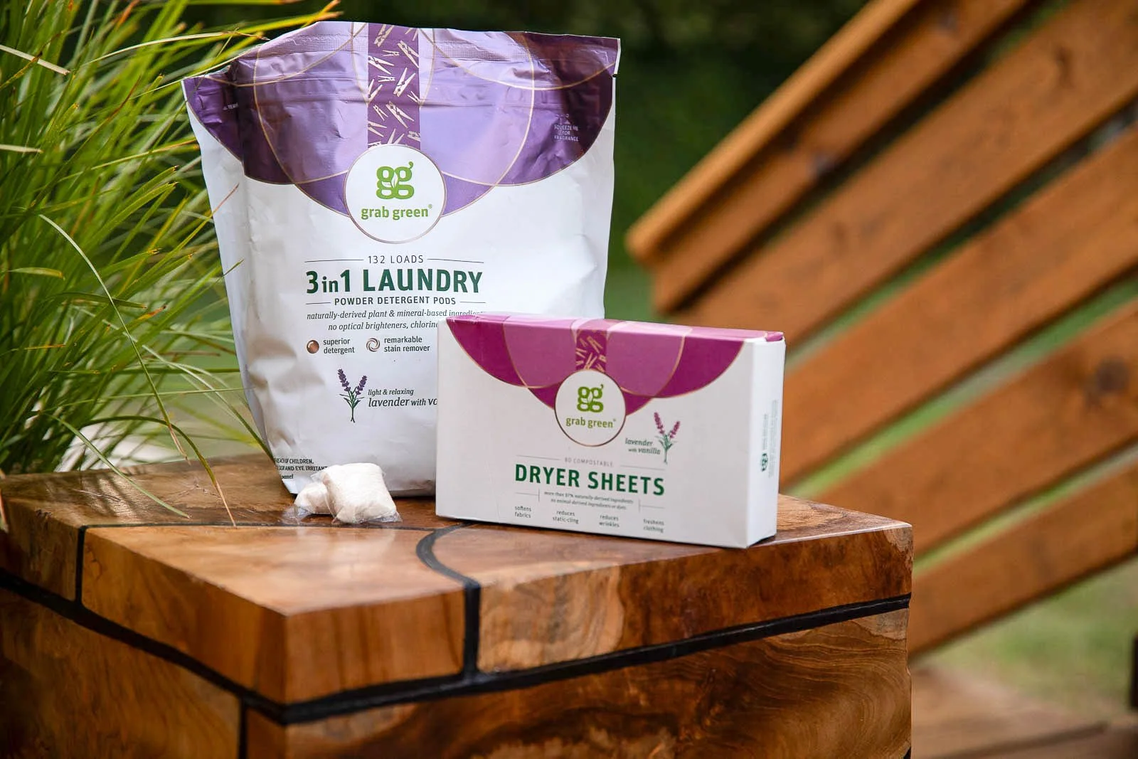 Laundry detergent powders and dryer sheets from Grab Green placed on a wooden surface outdoors.
