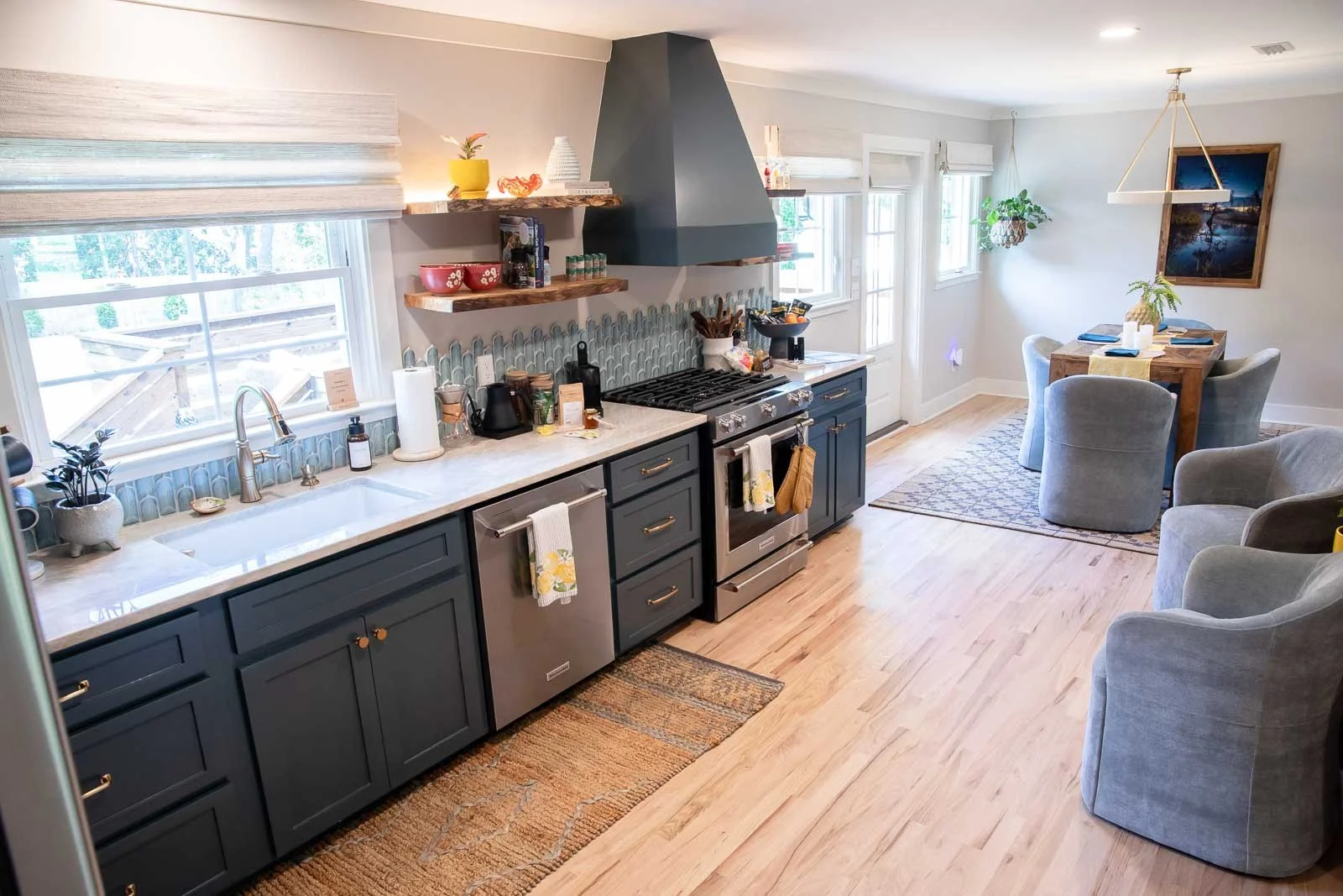 Open-concept kitchen and dining area with blue cabinets, stainless steel stove, and a round dining table with four light gray chairs.