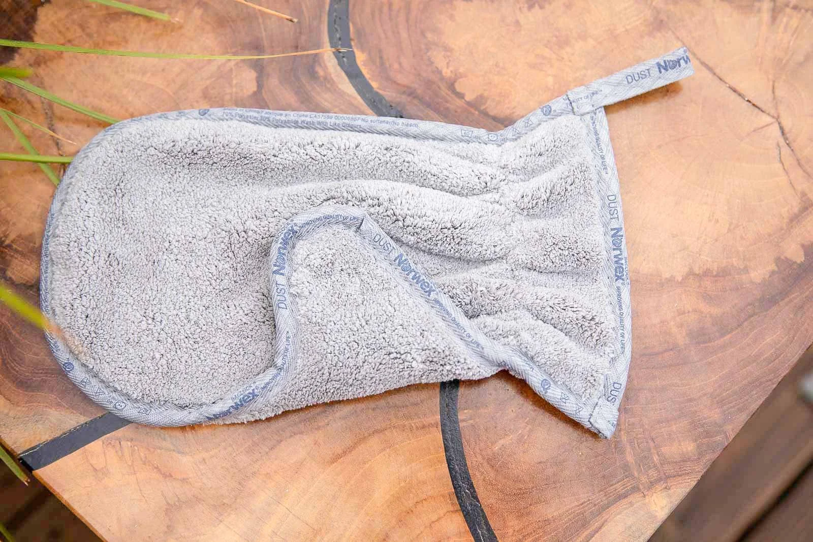 A used microfiber cleaning cloth lying on a wooden surface with visible grain patterns.