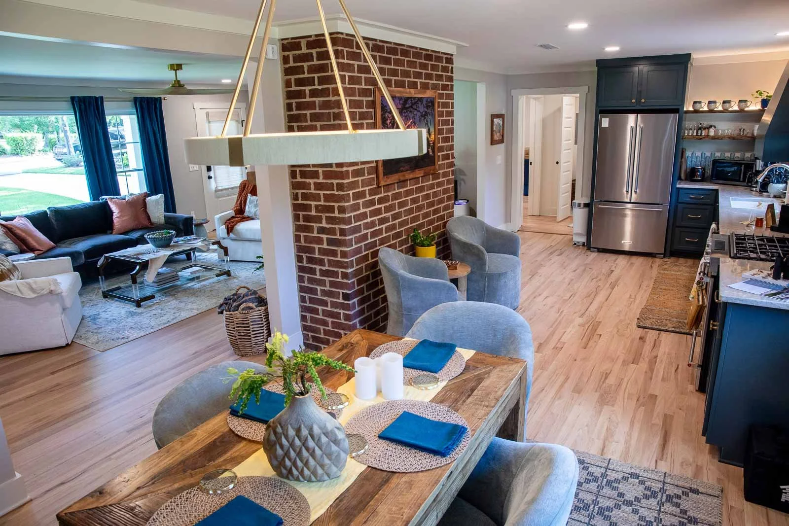 Open-concept living and dining area with a brick wall, dining table with place settings, a living room with couches, and a kitchen with stainless steel appliances.
