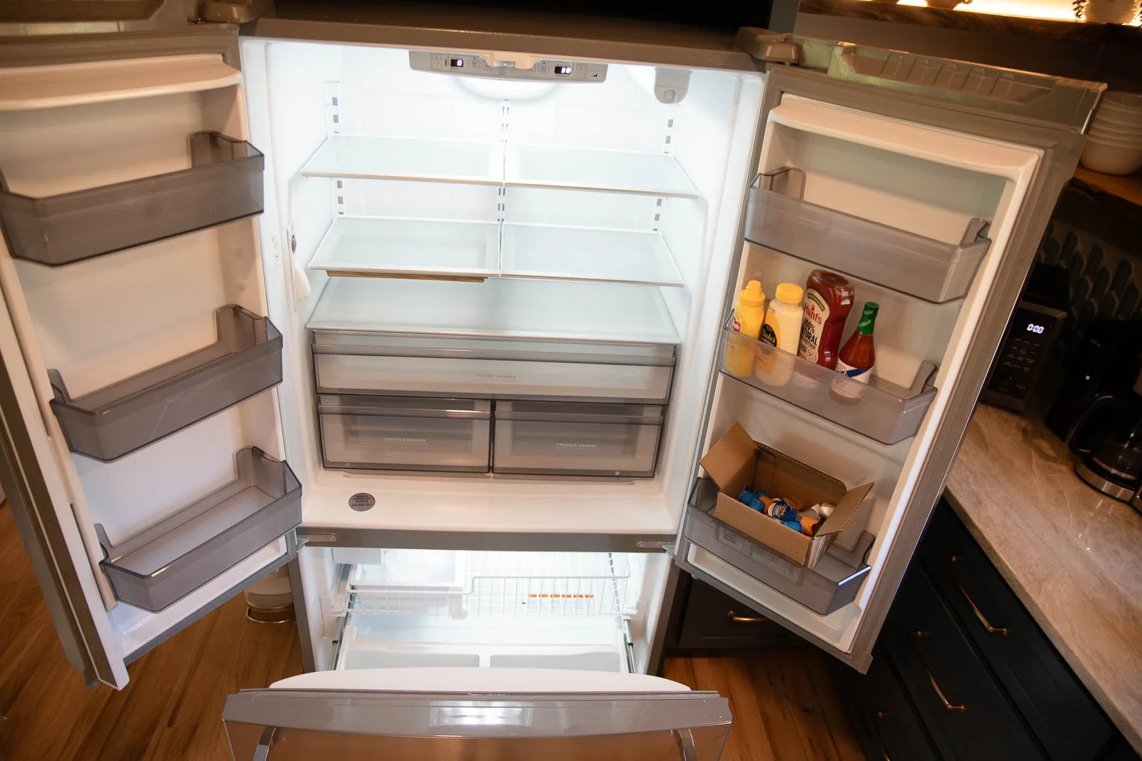 Empty refrigerator with a few condiment bottles on the door shelf and a box of chips on the lower shelf, with ocean background visible through a window.