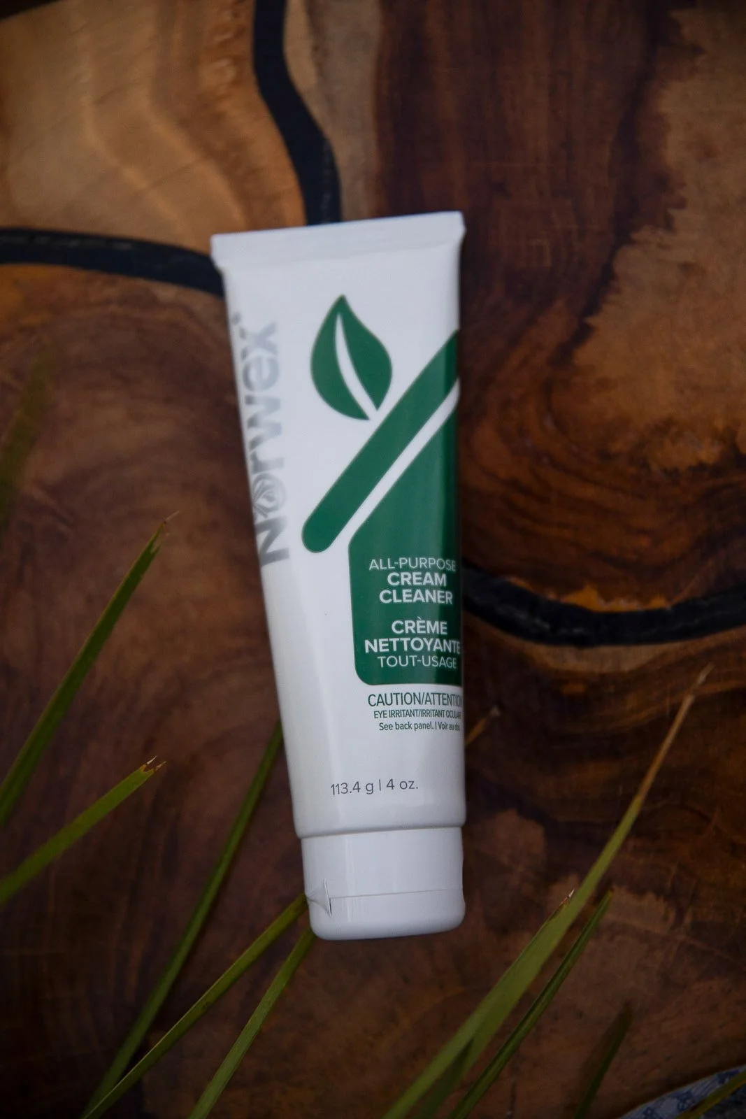 A tube of Neogen All-Purpose Cream Cleaner placed on a wooden surface with some green grass leaves nearby.