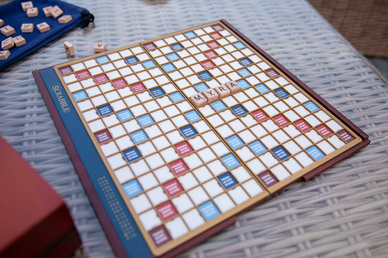 Scrabble board with the word 'MYRA' spelled out using letter tiles.