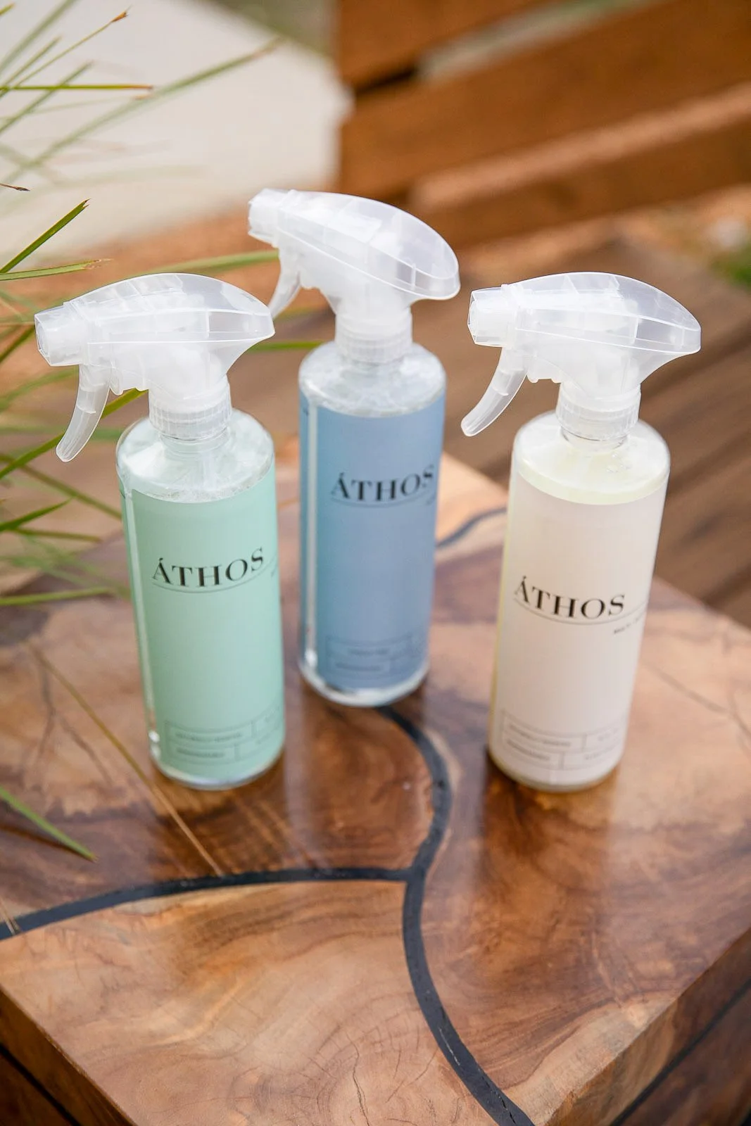 Three spray bottles labeled ÀTHOS in pastel colors (green, blue, and white) on a wooden surface with a natural wood grain pattern.