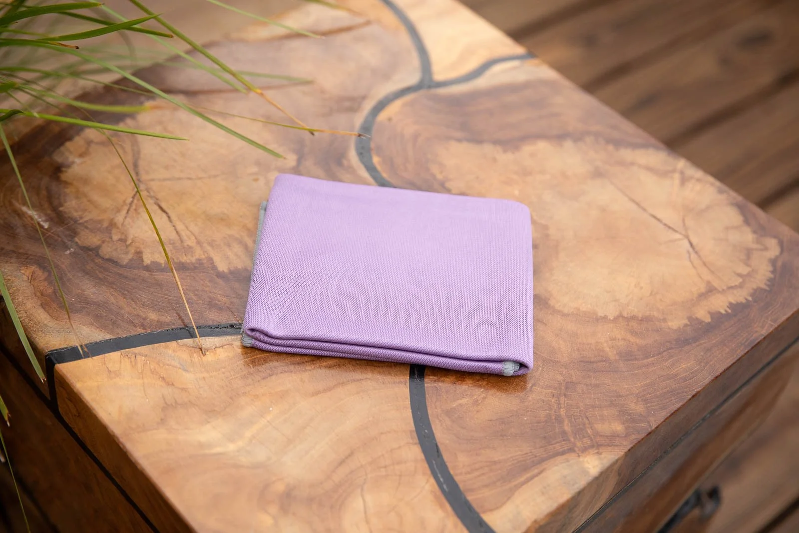 A folded lavender cloth napkin resting on a rustic wooden table with natural grain and black line accents.
