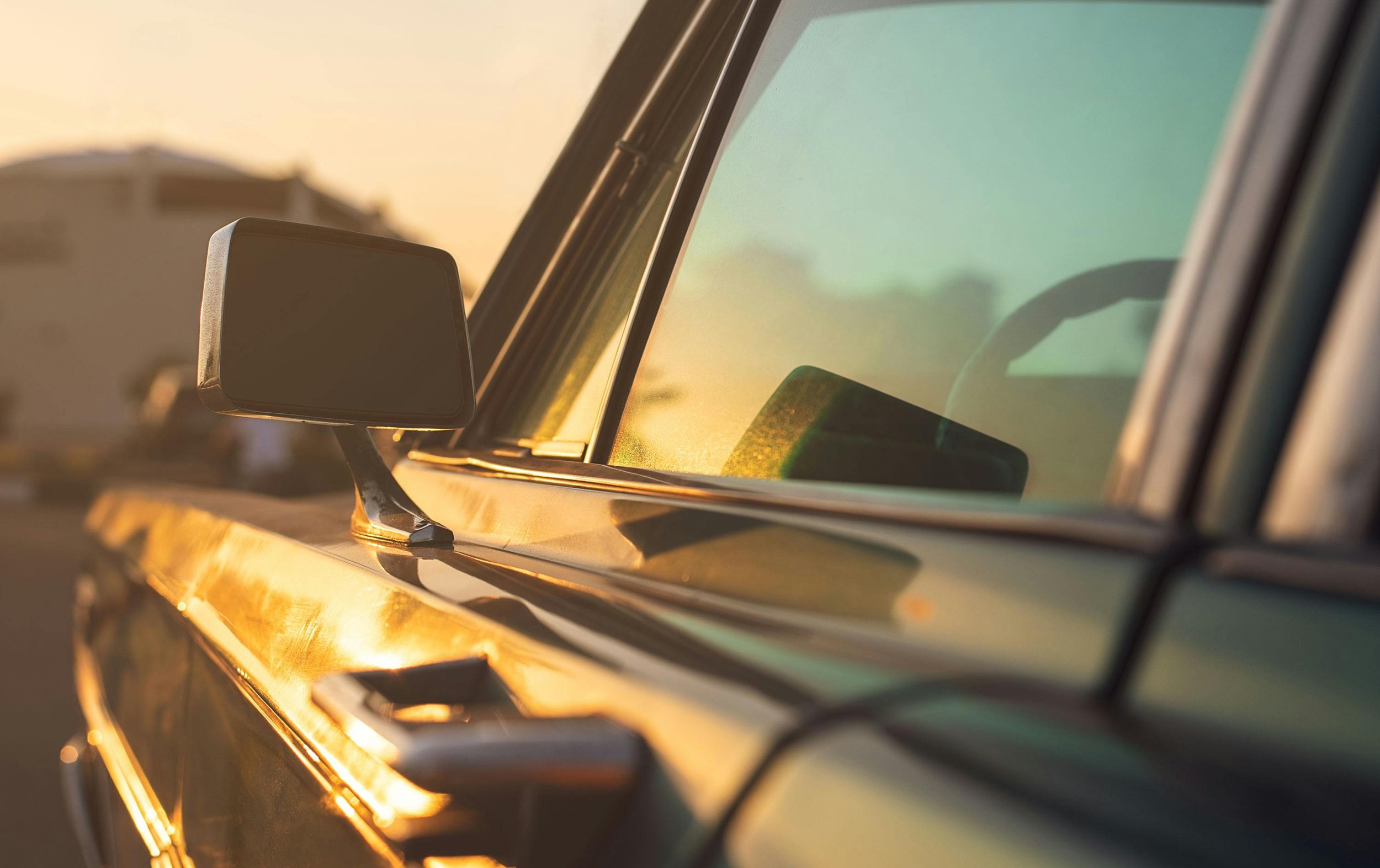 Close-up of a vintage car's side mirror and window, bathed in warm sunset light, with a blurred background.