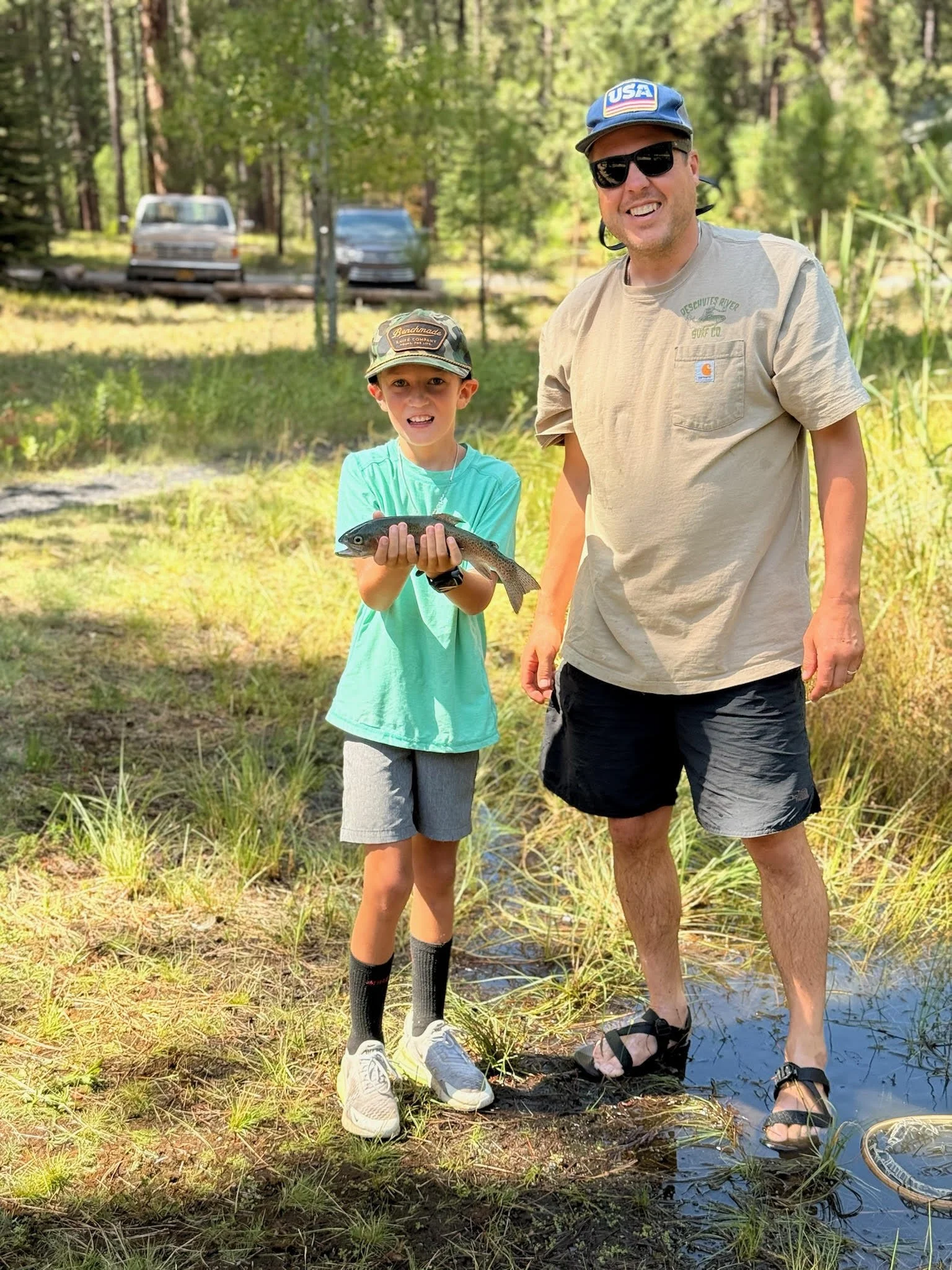 Justin Scott and friend Max holding a freshly caught trout at the stocked fishing pond at Lake Creek Lodge in Camp Sherman Oregon, a family-friendly fly fishing destination in the Metolius River valley of Central Oregon