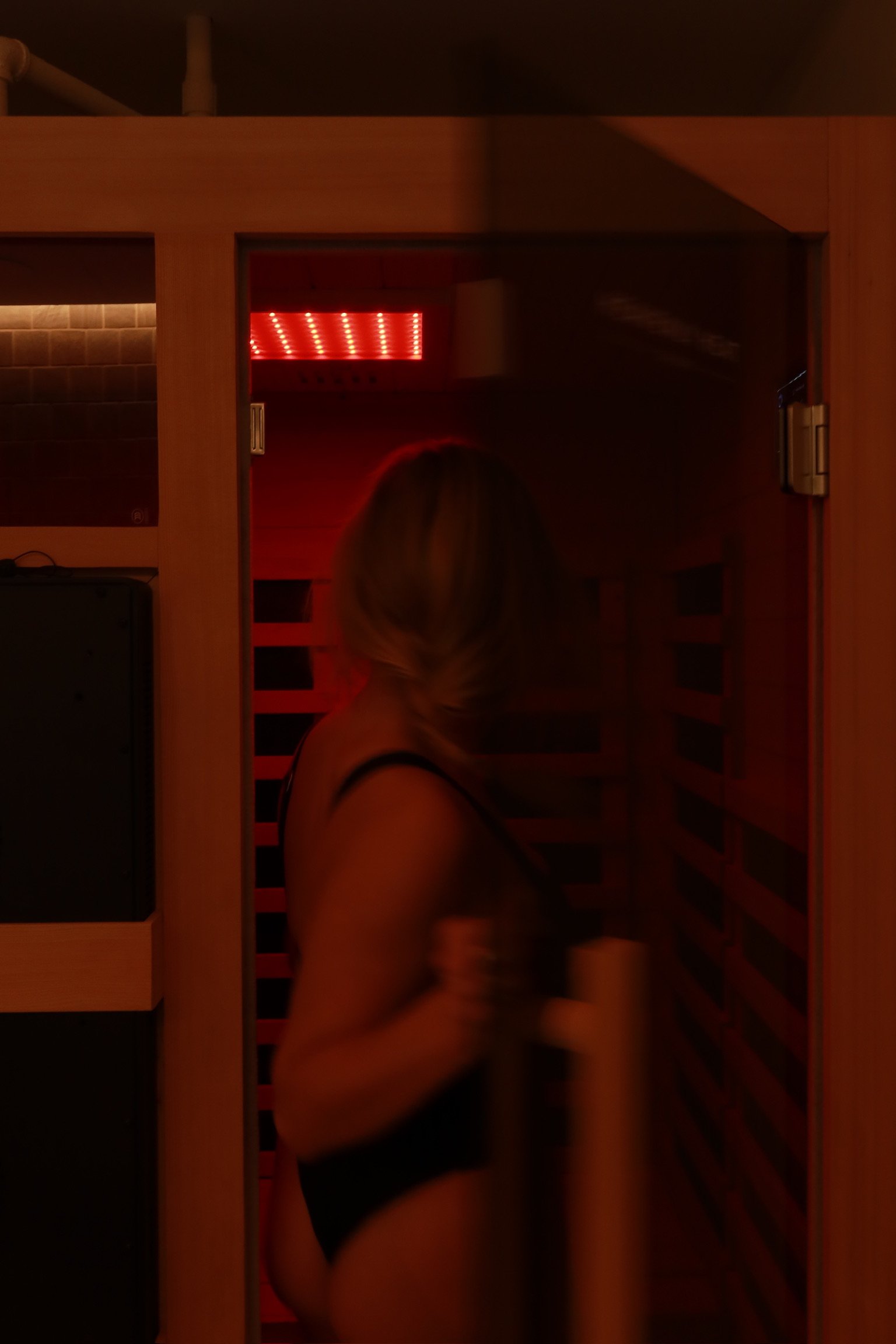 A woman in a black outfit inside a sauna room with red lighting.