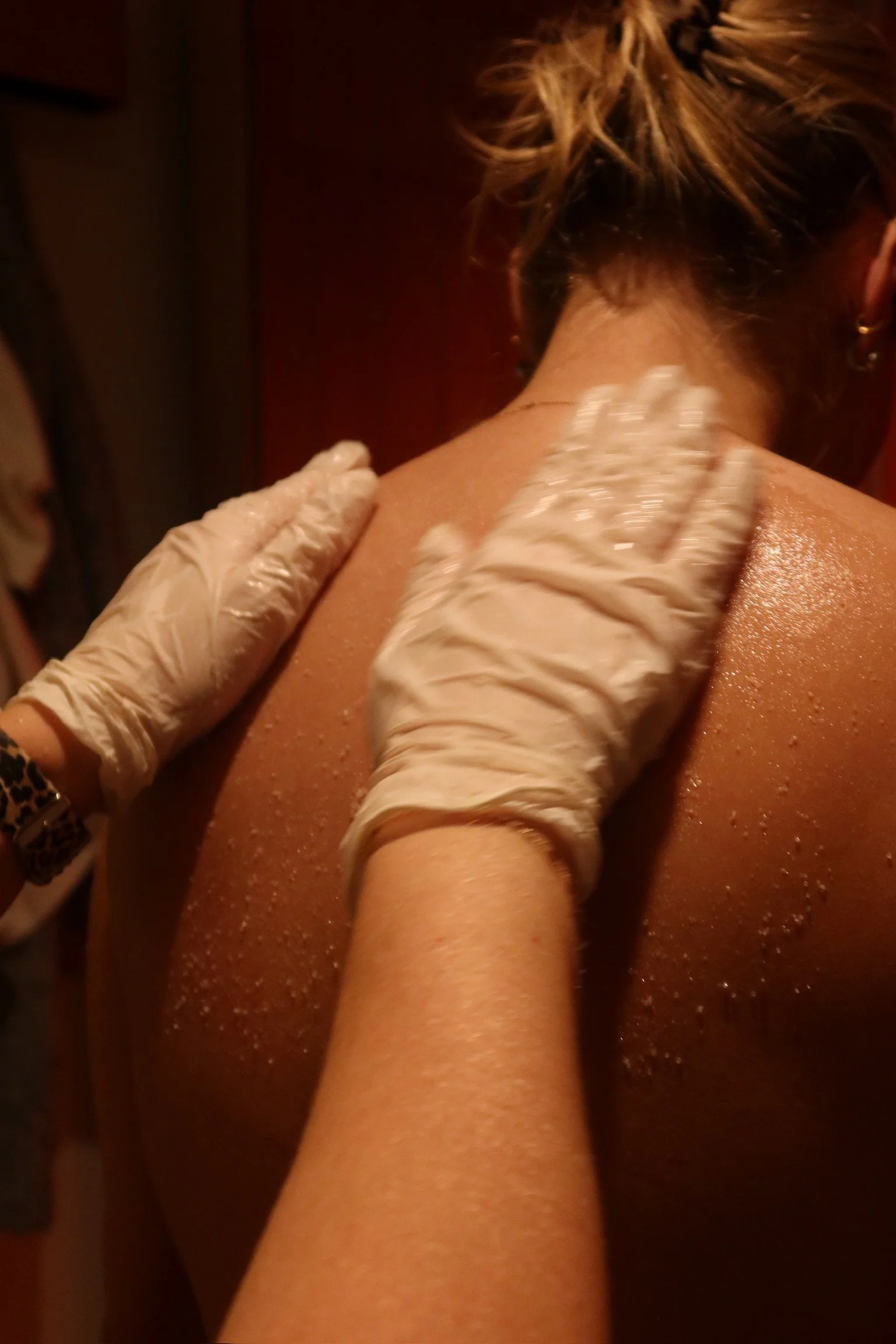 A person receiving a massage with gloved hands applying a scrub or lotion to their back.