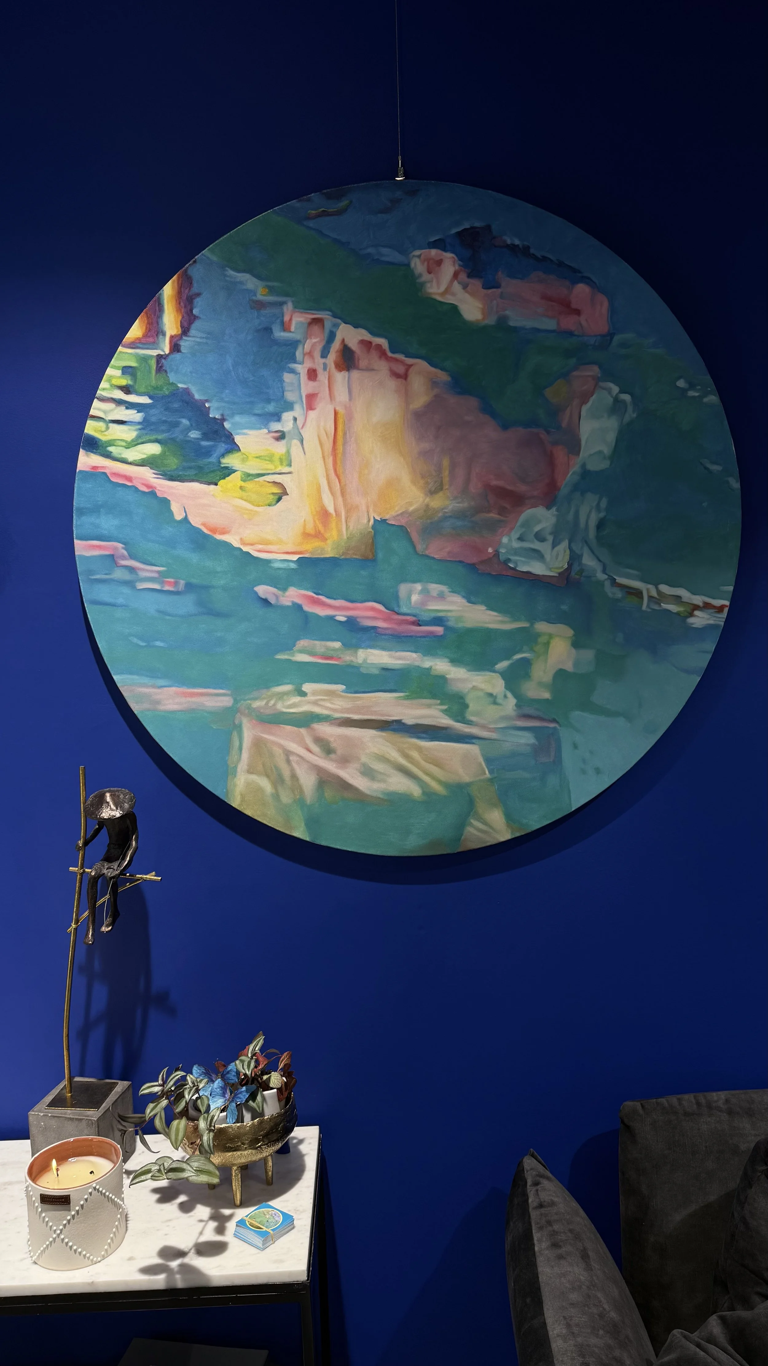 Peinture abstraite ronde avec des couleurs vives et des formes fluides, suspendue sur un mur bleu