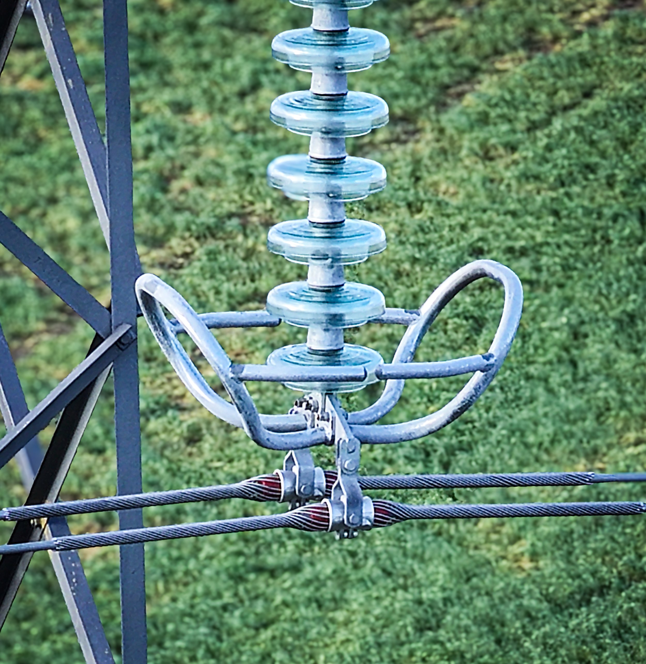 Close-up of a metal radio antenna with a glass insulator in a grassy outdoor setting.