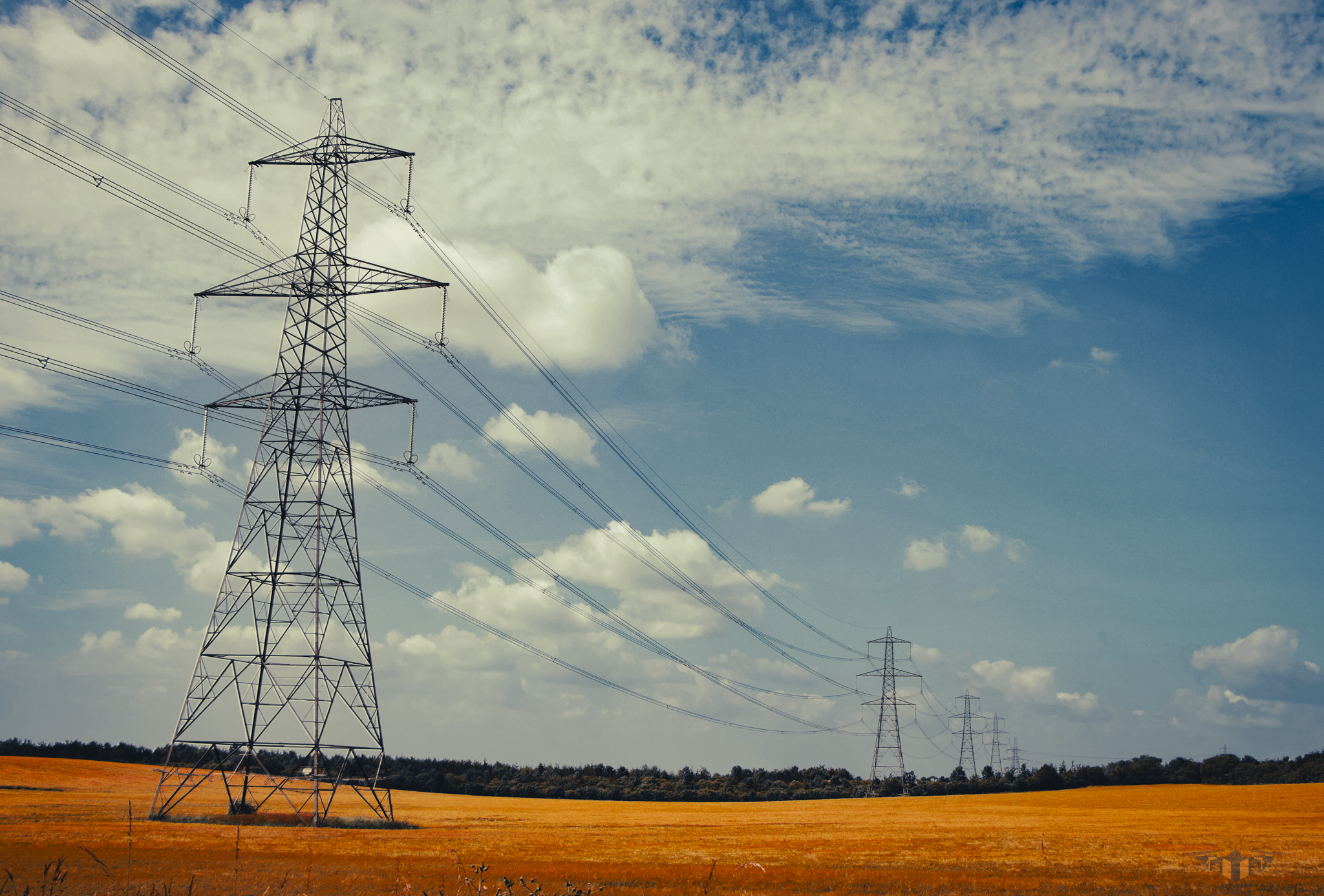 Electrical transmission towers and power lines in a field with a partly cloudy sky.