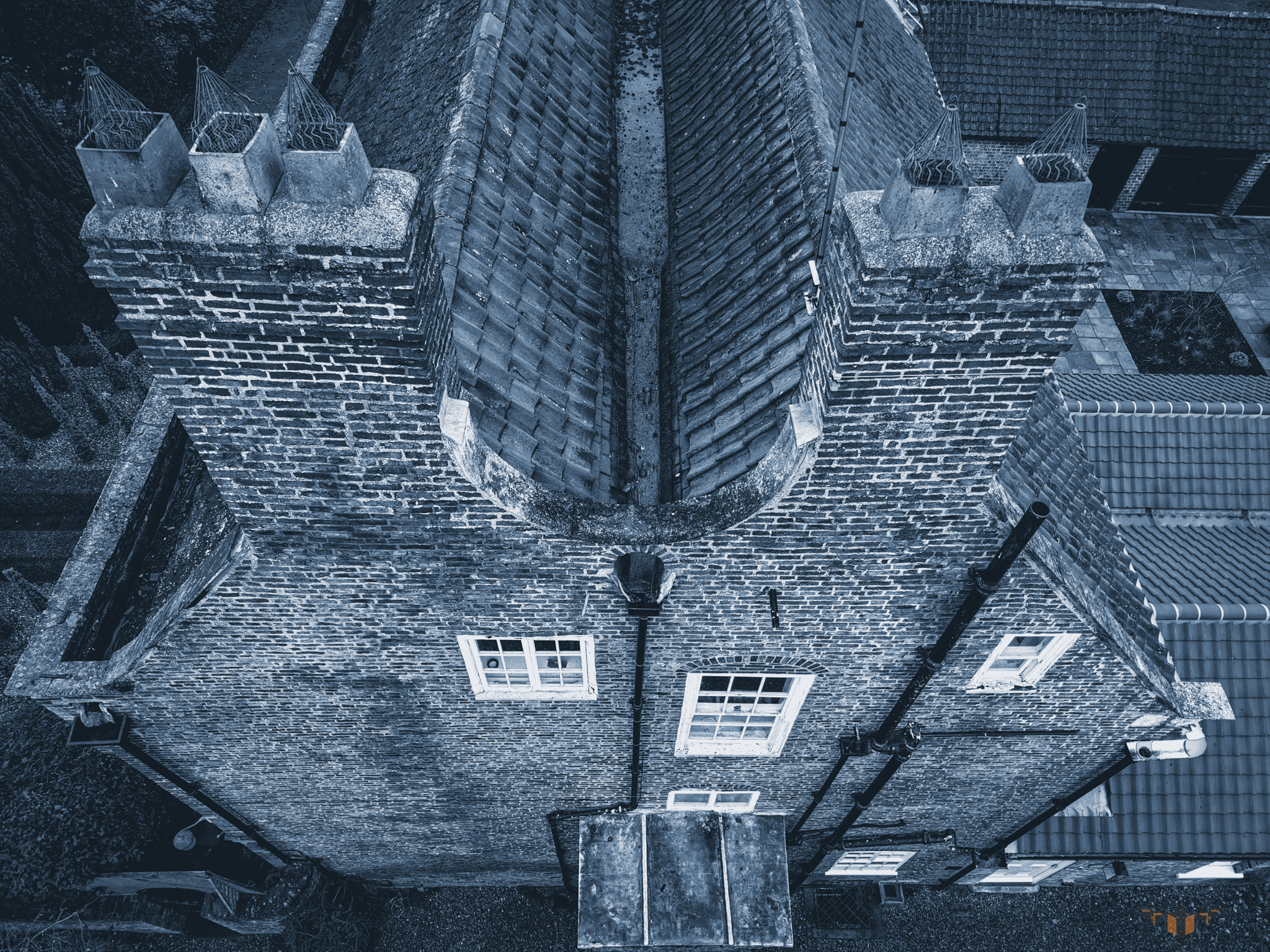 Aerial roof inspection showing a twin-pitch valley gutter between two brick chimney stacks, highlighting moss growth, debris build-up, and potential water drainage issues.