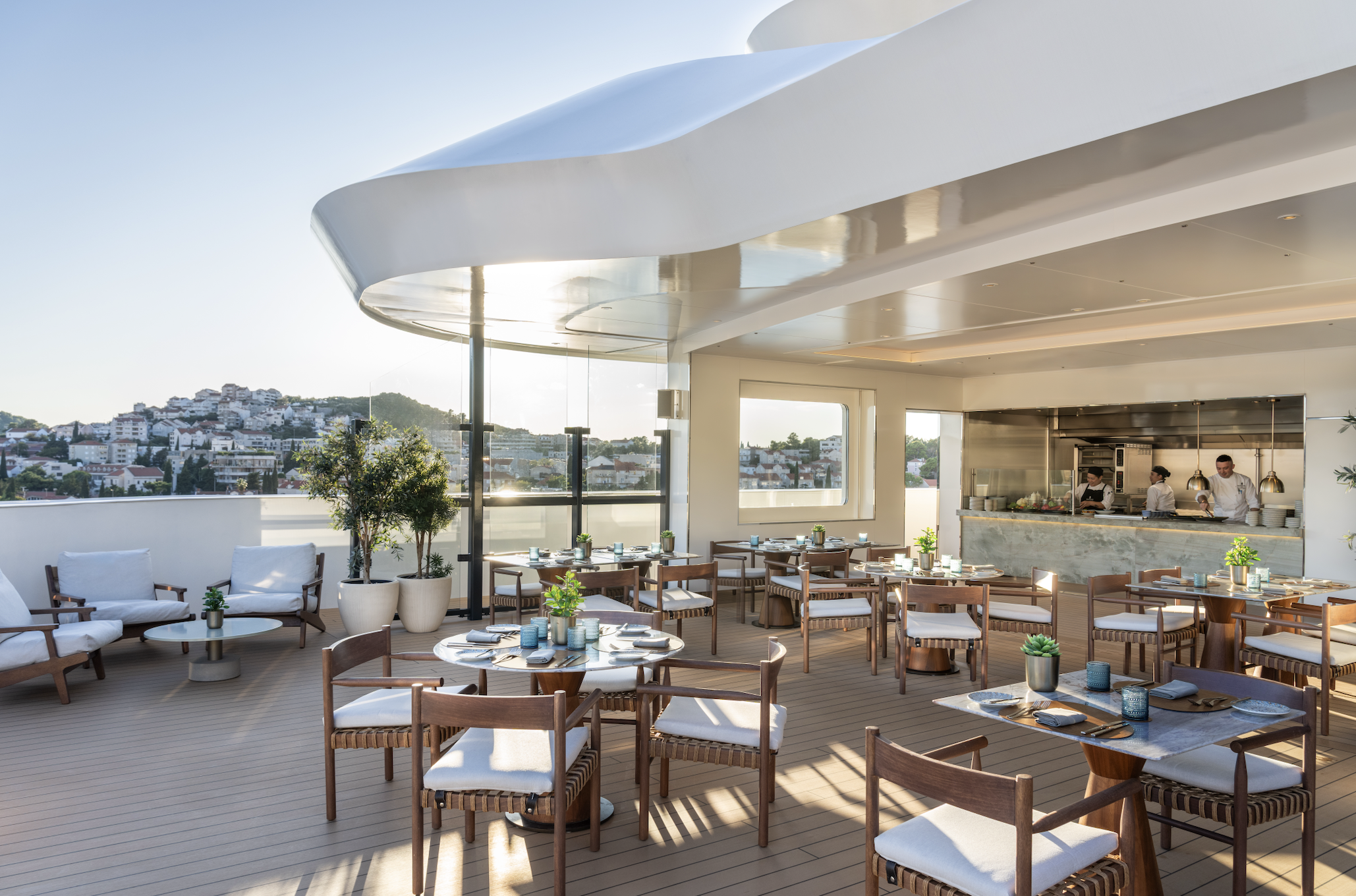 Outdoor dining terrace aboard The Ritz-Carlton Yacht Collection, featuring open-air seating and coastal views at sunset.