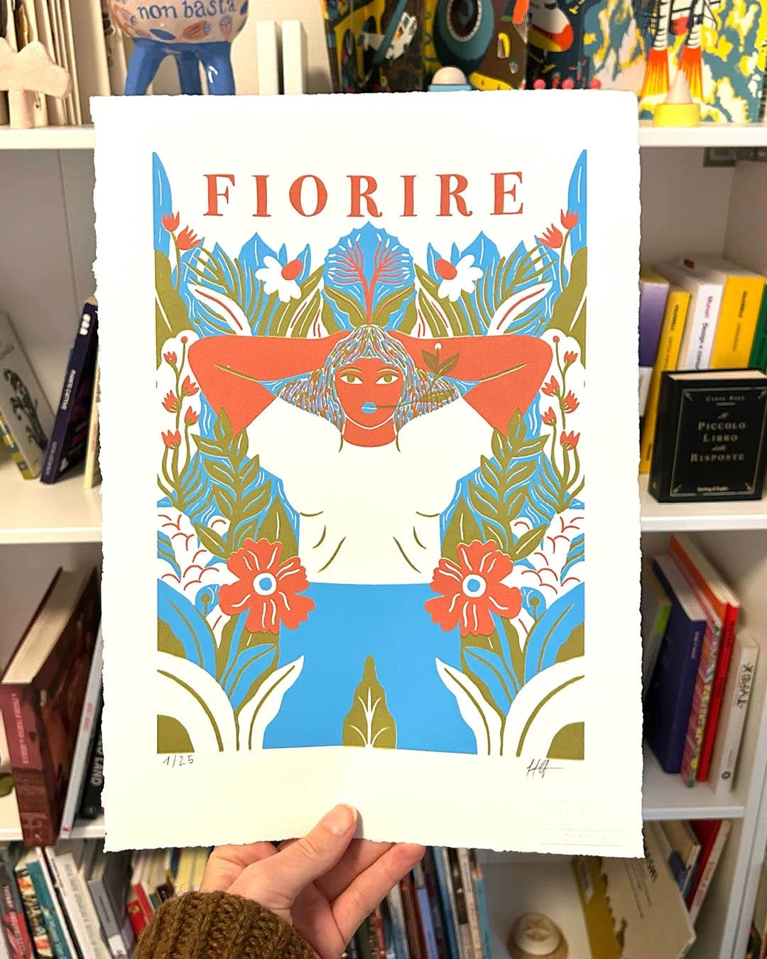 Poster artistico con illustrazione di una donna con capelli lunghi e vestita di bianco, circondata da foglie e fiori colorati, con il titolo 'FIORIRE' in alto.