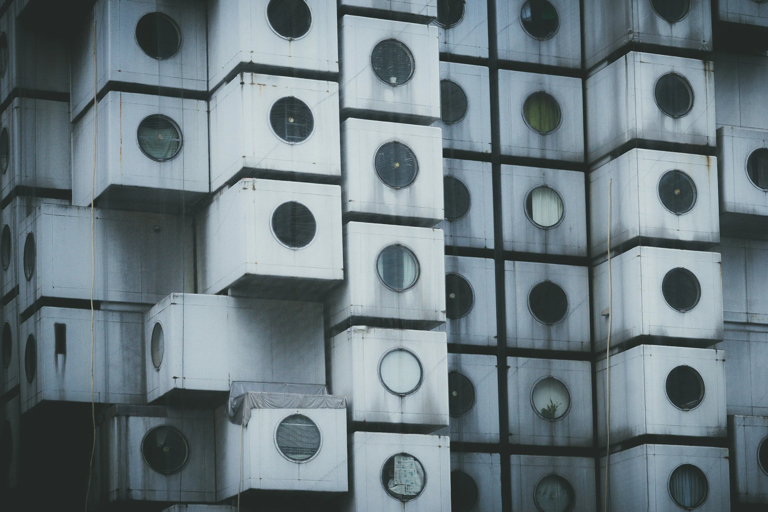 A building with multiple stacked outdoor laundry drying machines or air conditioning units, each with a circular window, arranged in a grid pattern.