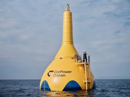 Yellow underwater buoy with 'CorPower Ocean' logo floating on the ocean surface, with a person standing on it and a blue sky overhead.