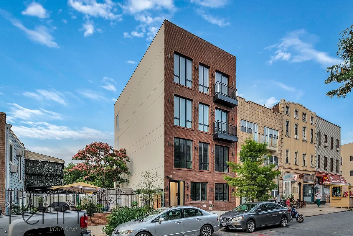 Street view of brick buildings, one with a fire escape and a 'For Lease' sign, scaffolding on the right, and a car parked in front.