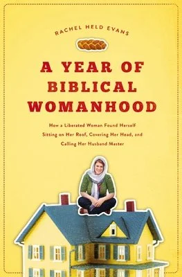Book cover of 'A Year of Biblical Womanhood' by Rachel Held Evans, featuring a small house and a woman sitting cross-legged on the roof against a yellow background.